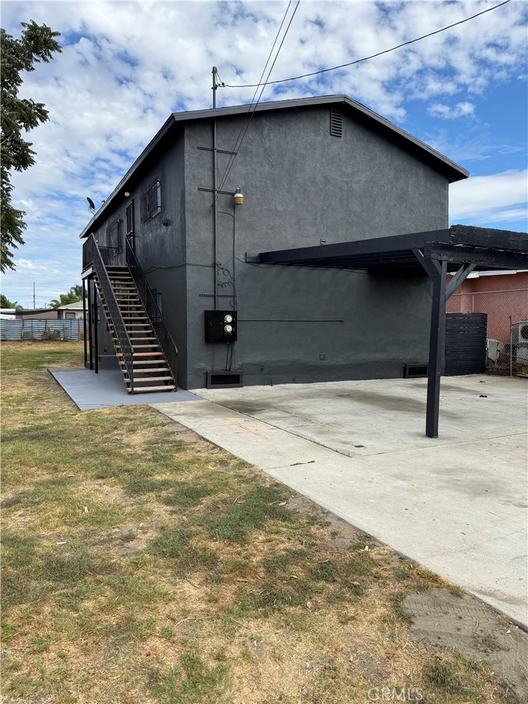 Dark gray two-story building with an exterior staircase and covered concrete parking area.