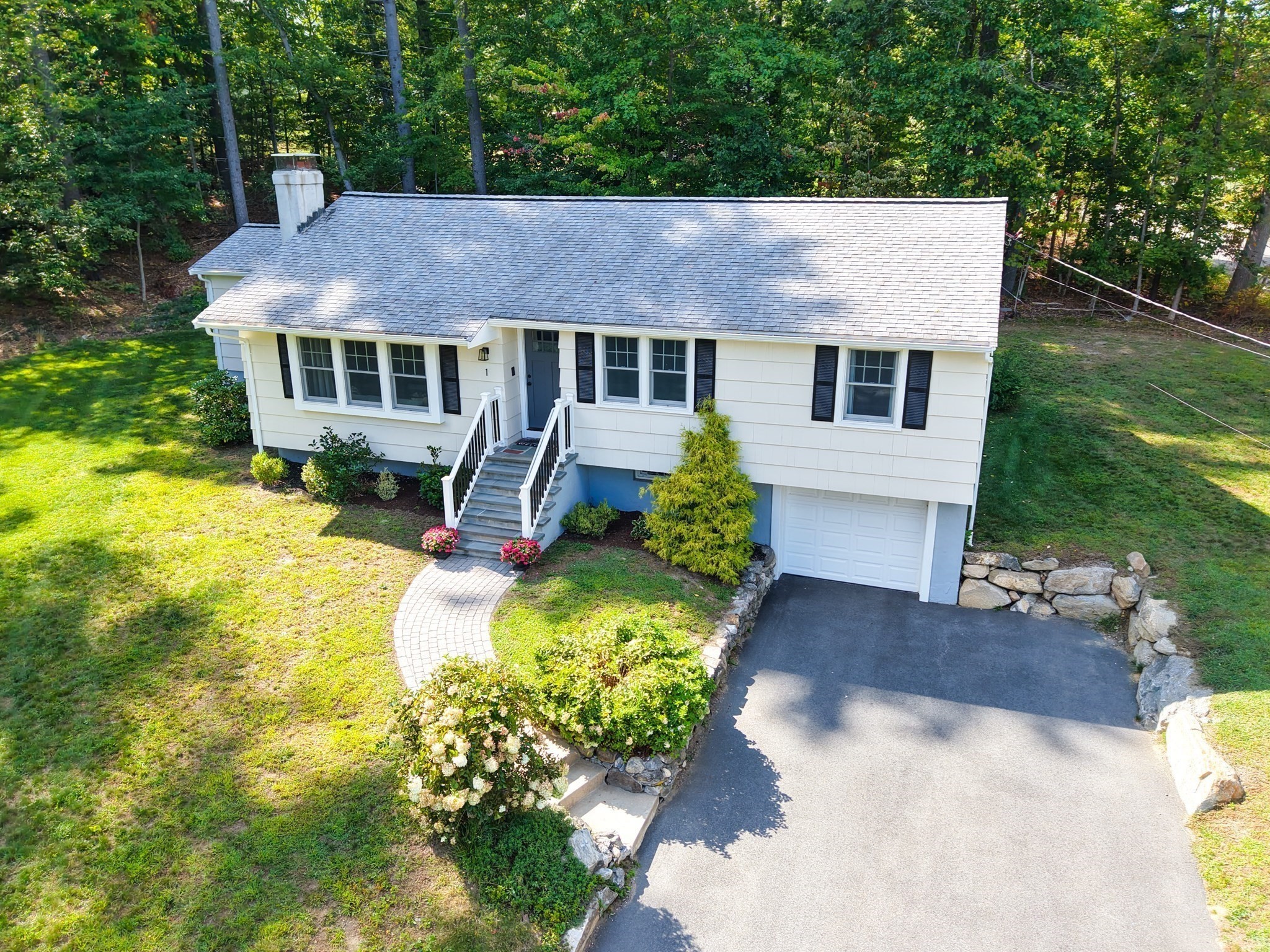 White split-level home with black shutters, front steps, attached garage, and a landscaped yard.