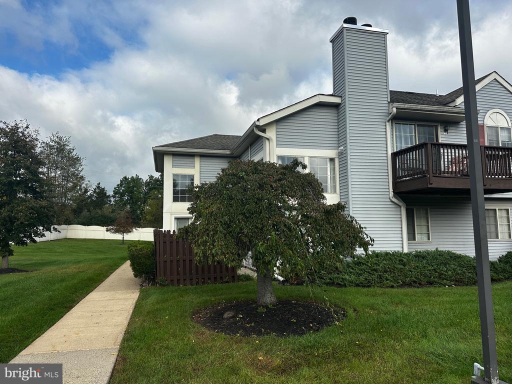 Gray-sided home with a dark wooden balcony, chimney, landscaped lawn, and walkway.