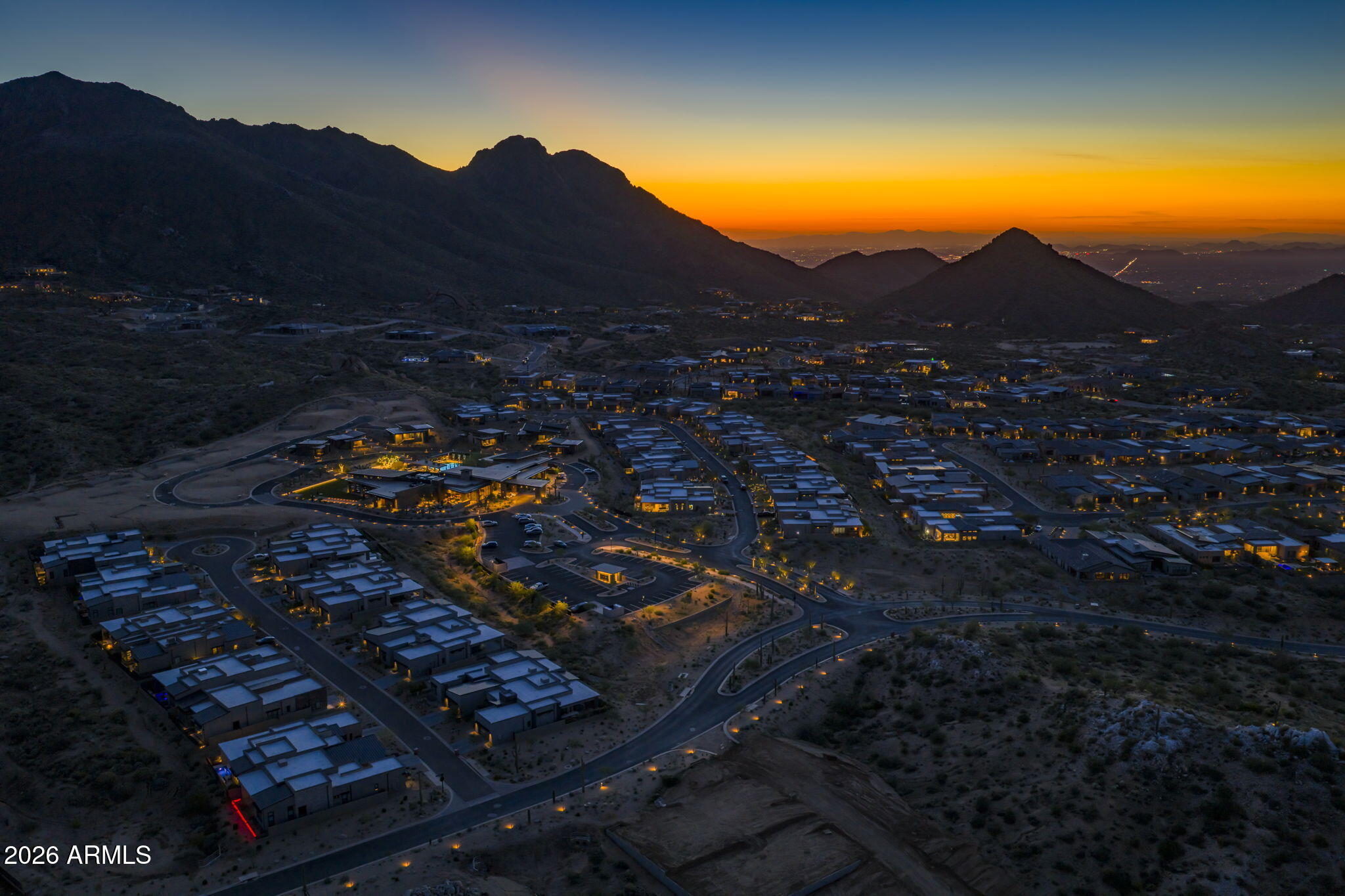 Aerial view of a desert residential community and winding roads beneath mountains at sunset.