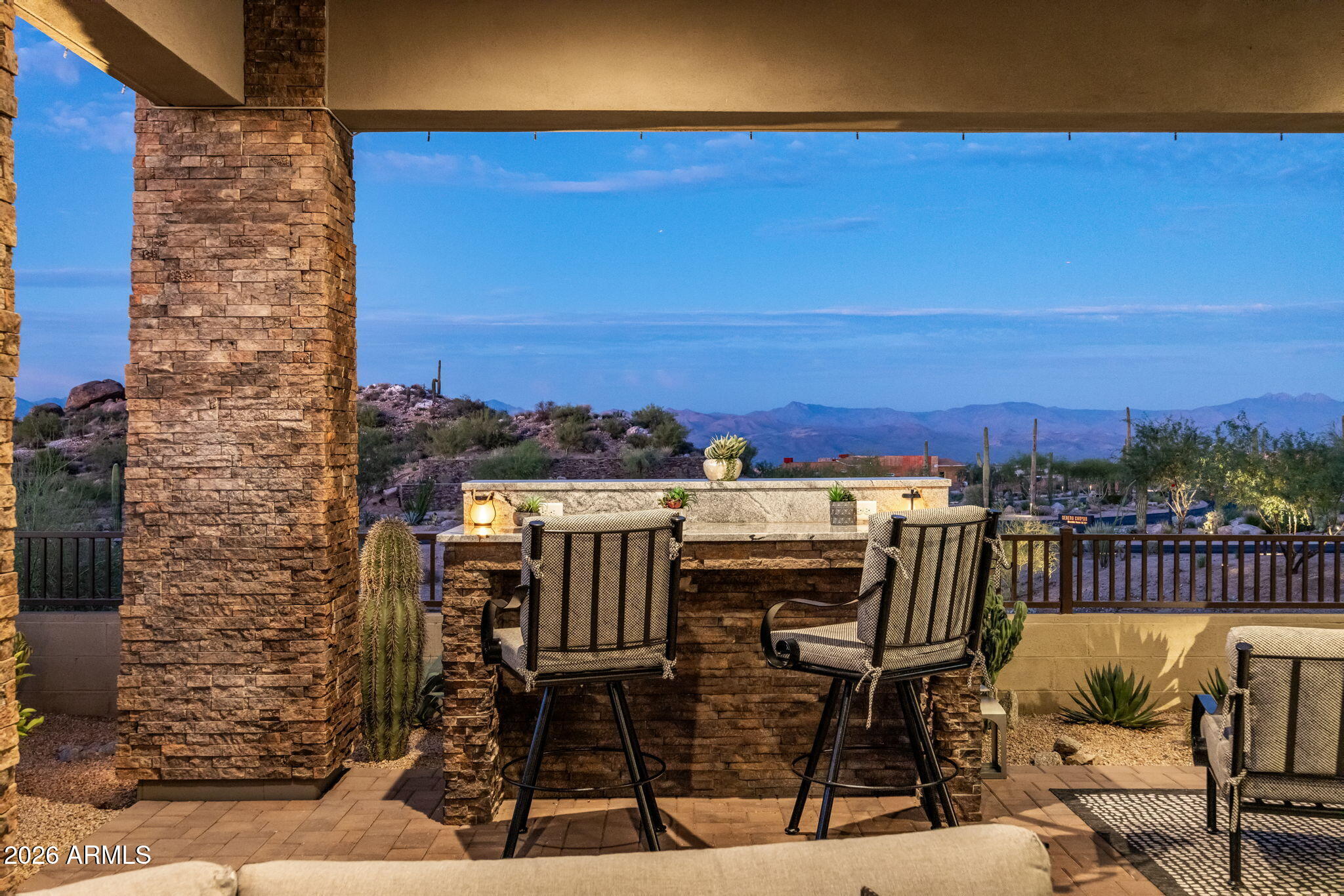 Covered stone patio bar with tall chairs overlooking desert hills and distant mountains.