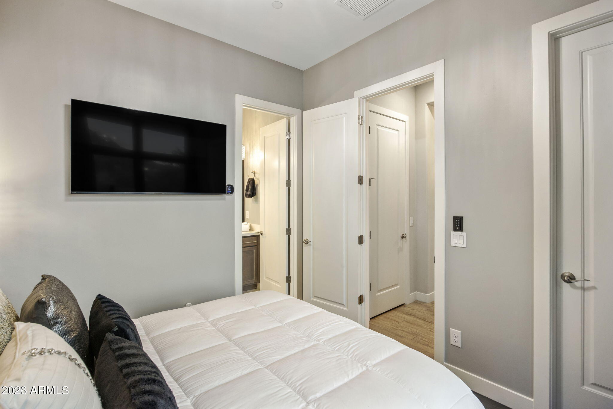 Bedroom with a white bed, dark accent pillows, and a large wall-mounted television.