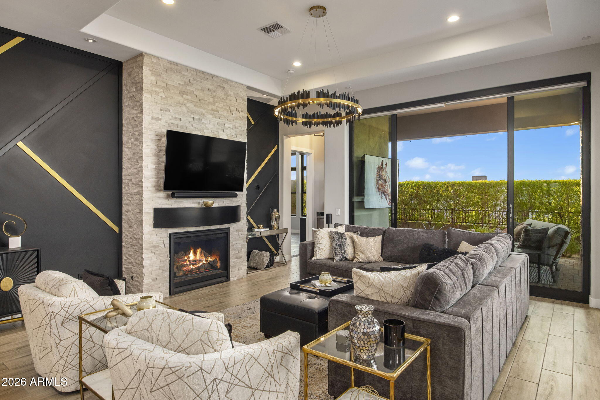 Modern living room with a stone fireplace, gray sectional, and sliding doors to a hedge-lined patio.