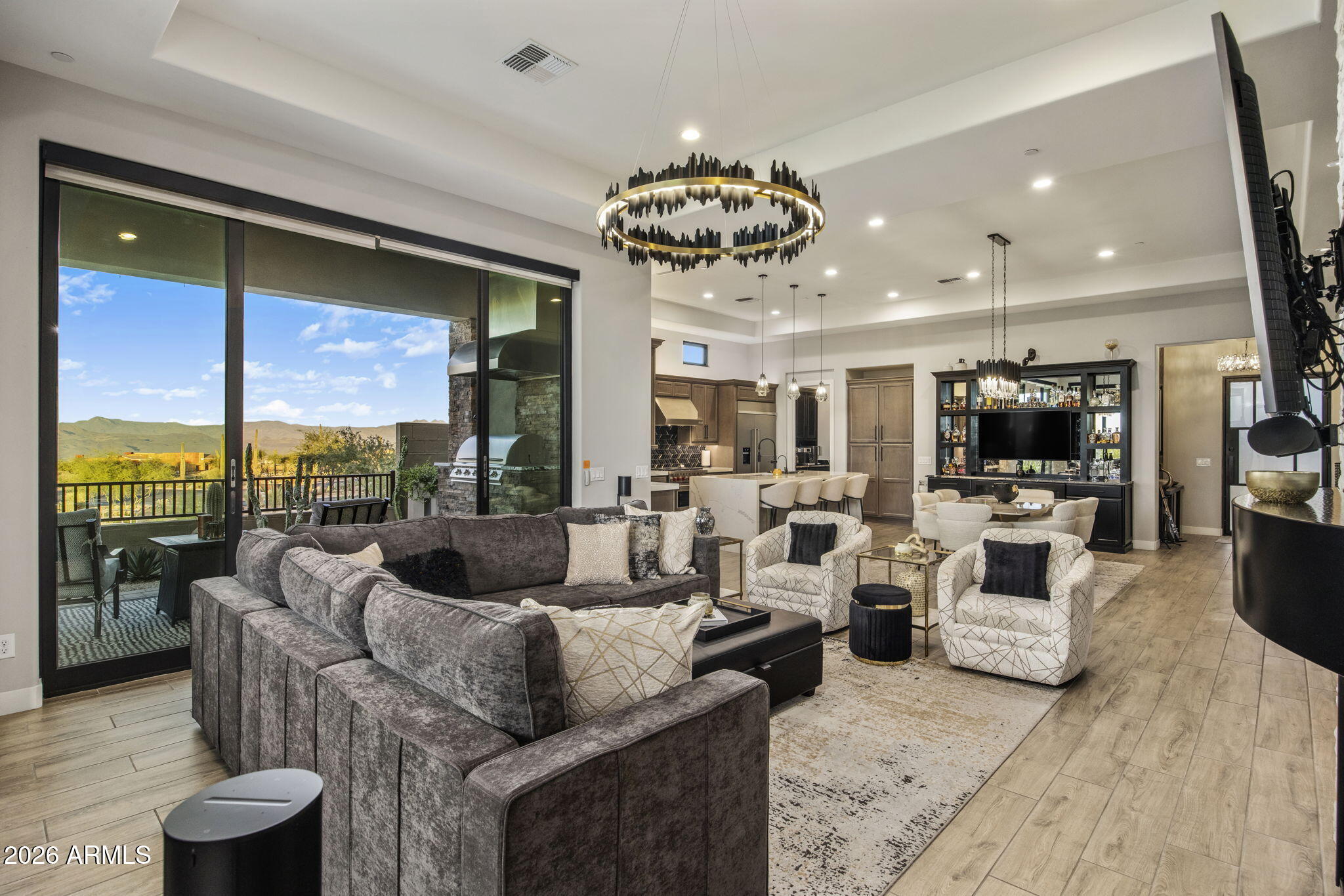 Open-plan living room with a gray sectional, circular chandelier, and sliding doors overlooking distant mountains.