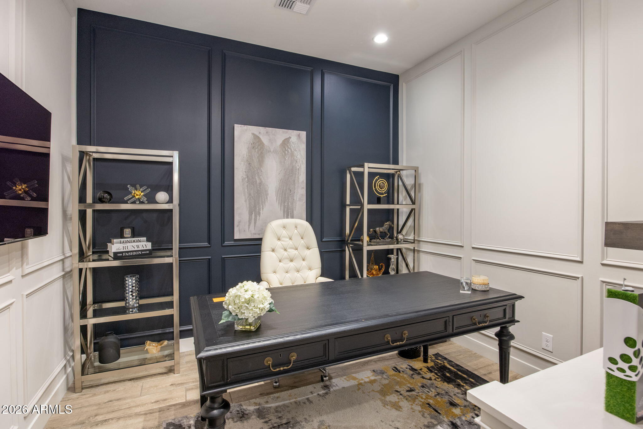 Furnished home office with a dark desk, cream chair, and navy paneled accent wall.