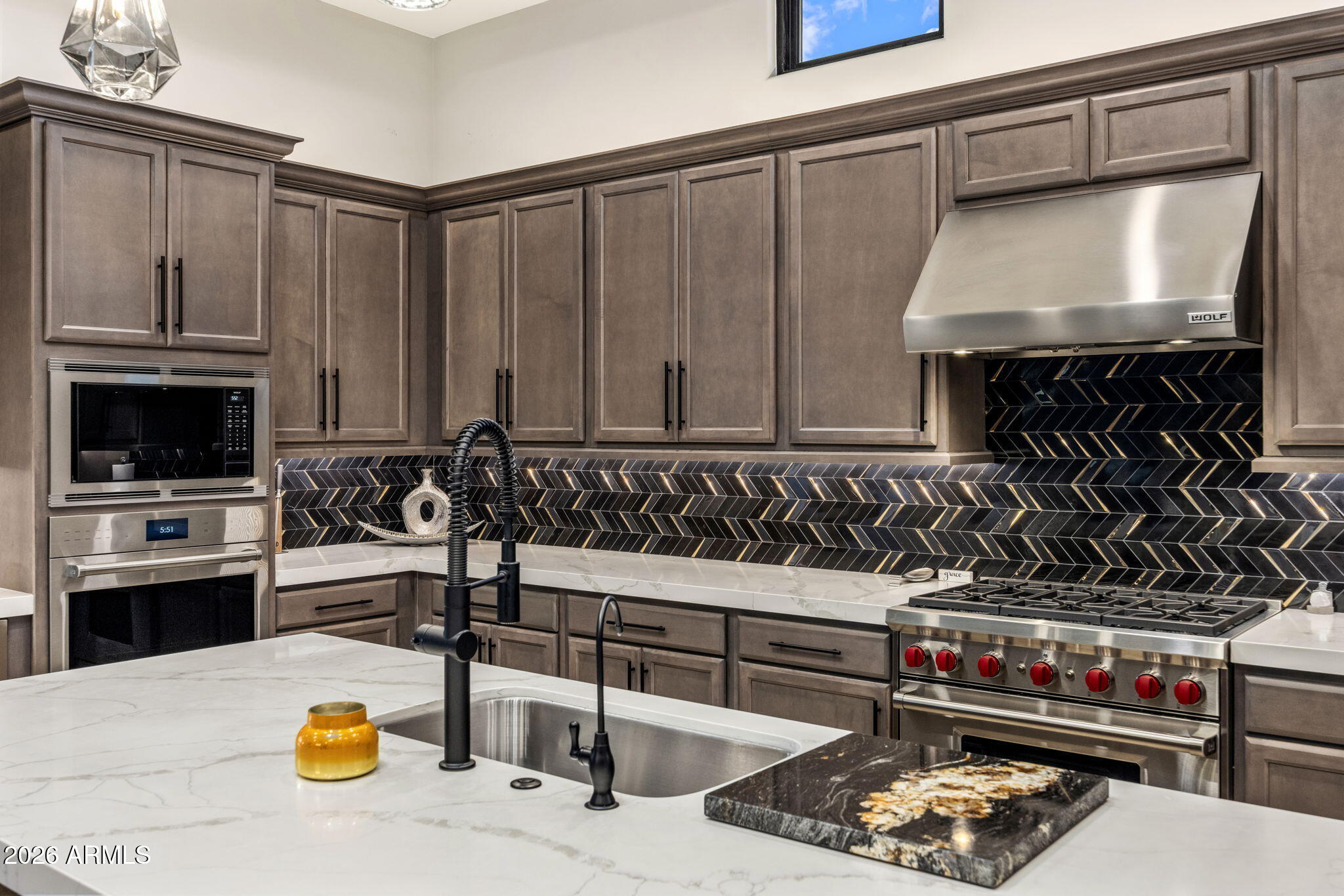 Kitchen with a black-and-gold herringbone backsplash, marble island, and stainless Wolf range.
