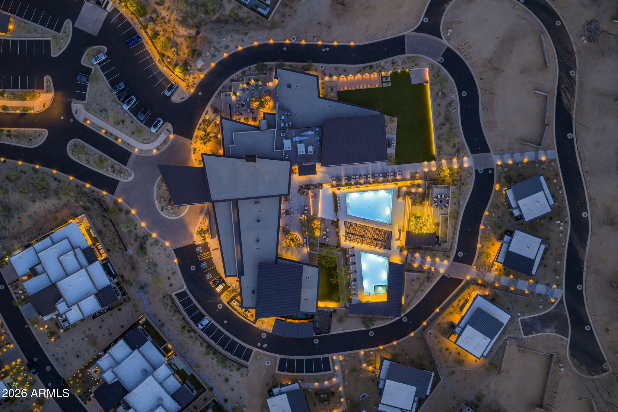 Aerial view of a modern property with two illuminated pools and curving roads.