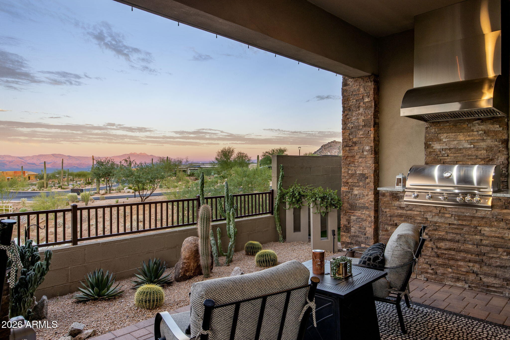 Covered patio with built-in grill, desert landscaping, and distant mountain views at sunset.