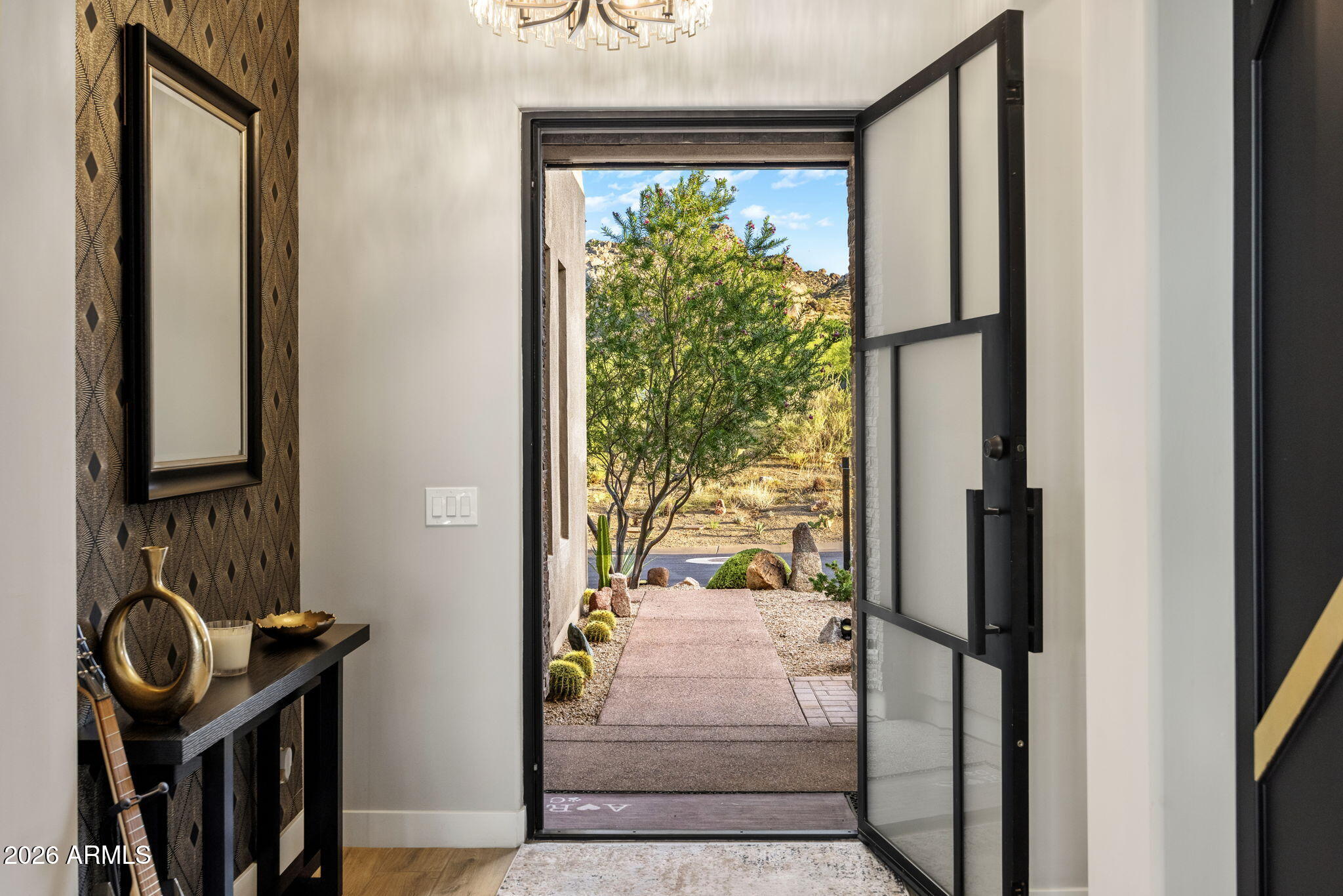 Entryway with an open black-framed glass door overlooking a desert garden path and rocky hills.