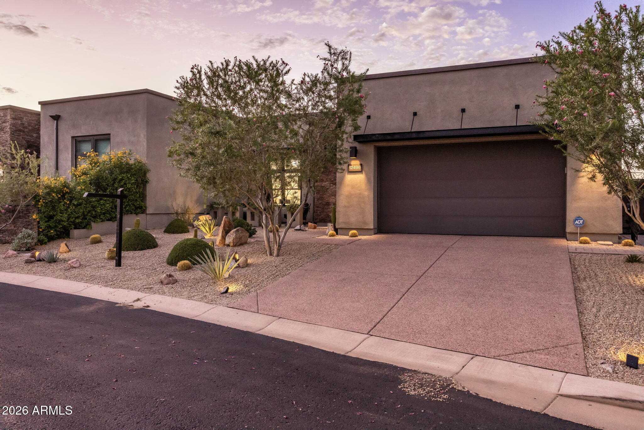 Modern stucco home with a broad garage, desert landscaping, and mature flowering trees.