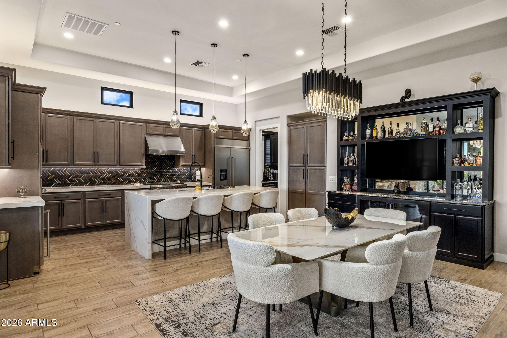 Open-plan kitchen and dining area with a marble island, dark cabinetry, and a built-in bar and TV cabinet.