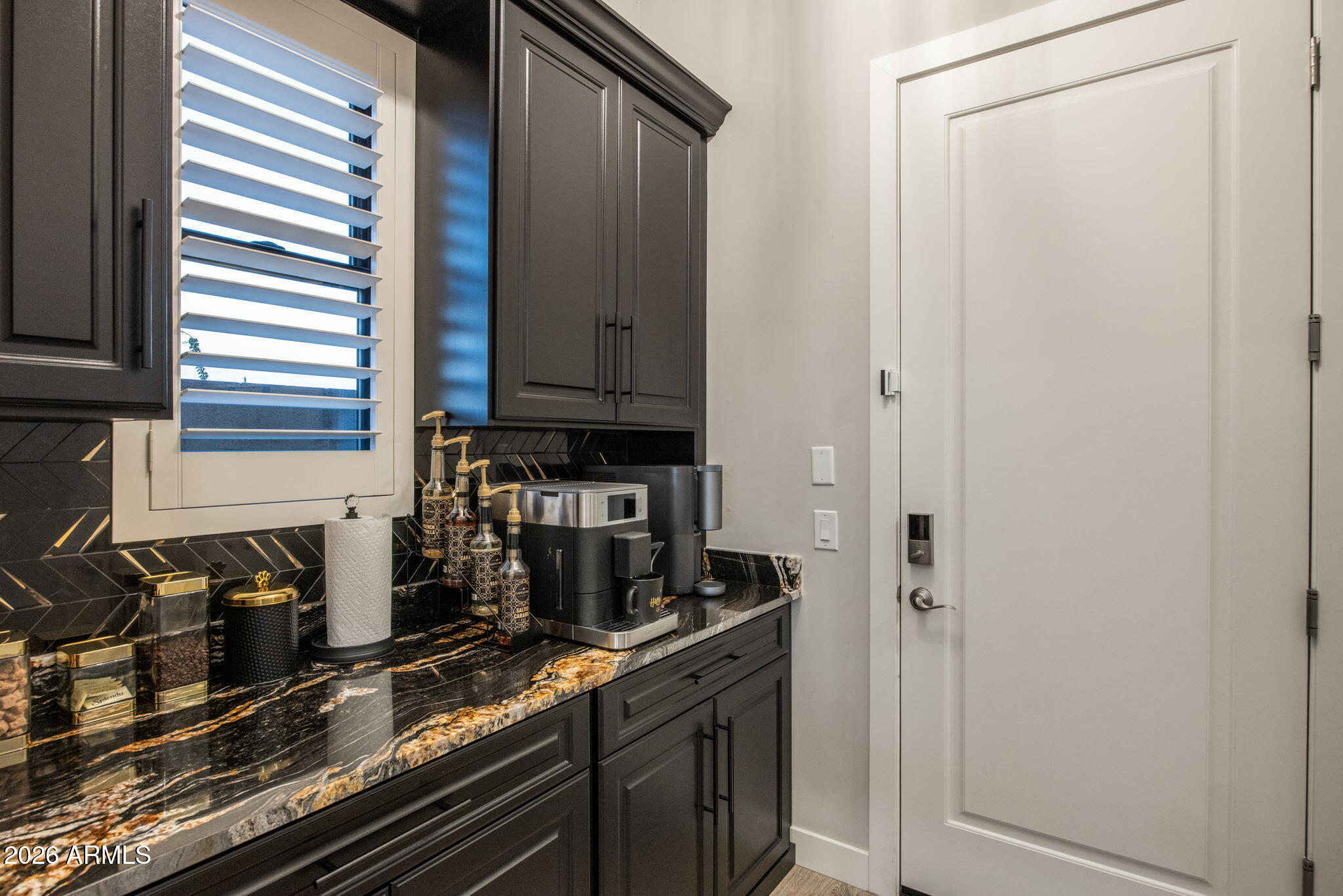 Built-in coffee bar with dark cabinetry, black-and-gold stone counters, and an espresso machine beside a white door.