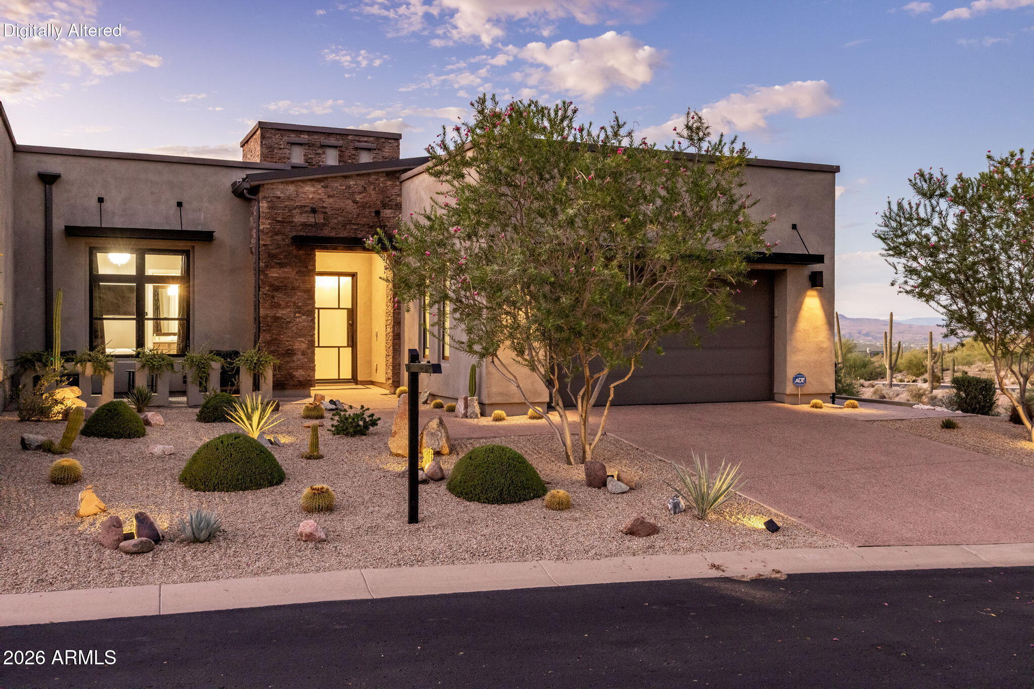 Modern stucco home with stone entry, desert landscaping, and distant mountains at dusk.