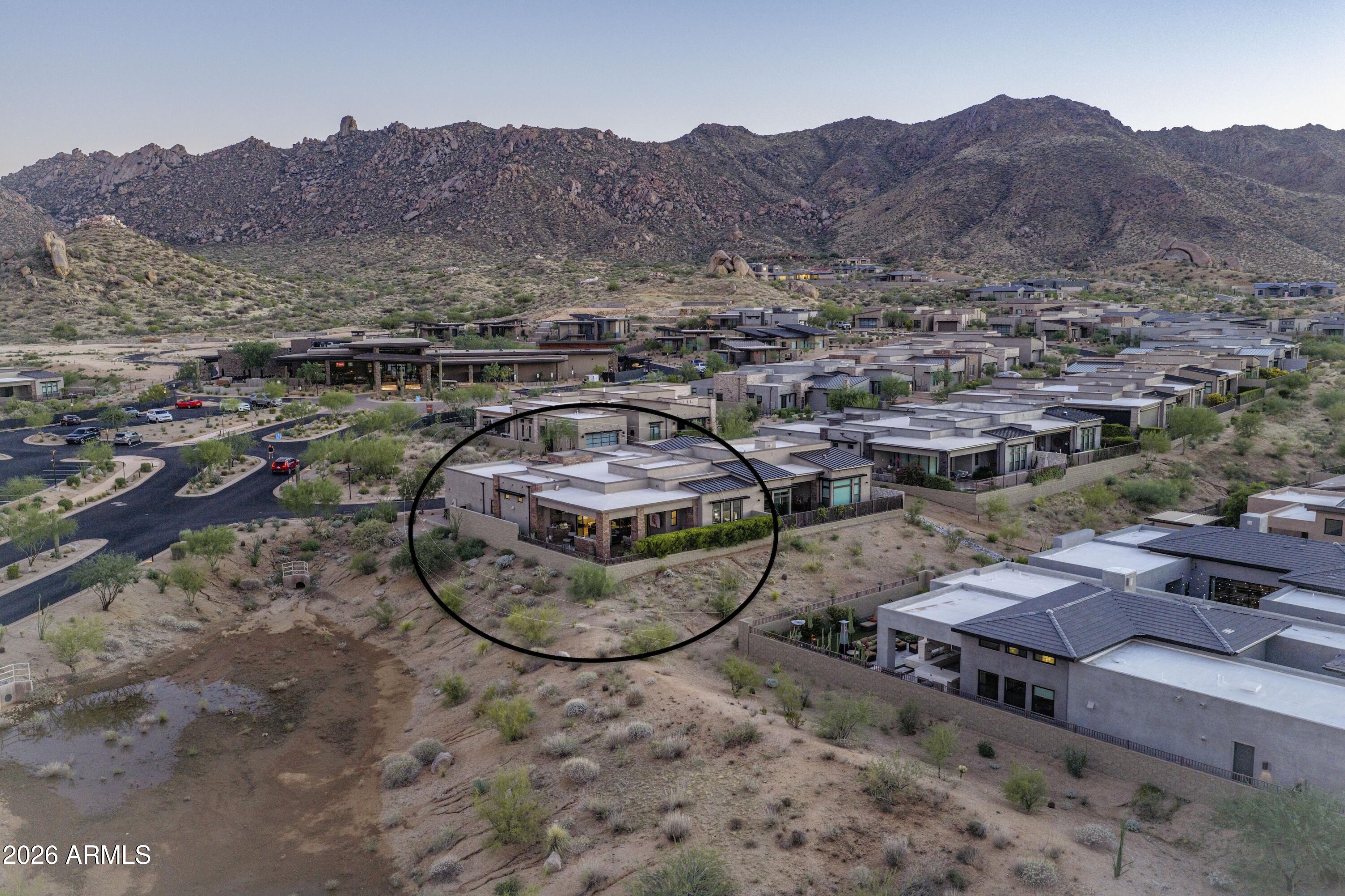 Circled modern desert home among neighboring residences, with rocky mountains in the background.