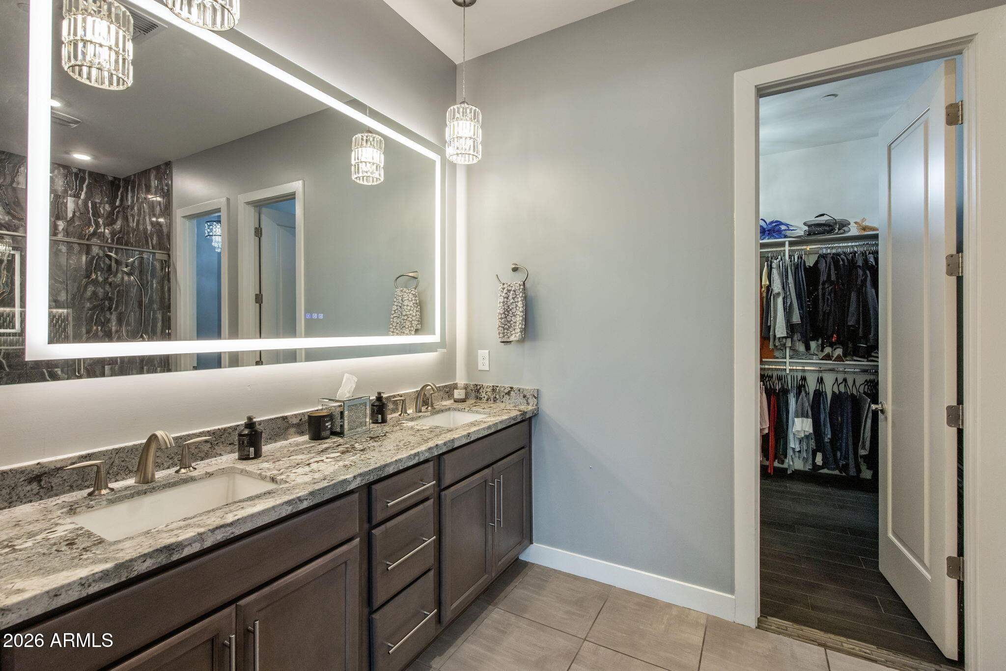 Modern double-sink bathroom vanity with an illuminated mirror and open walk-in closet.