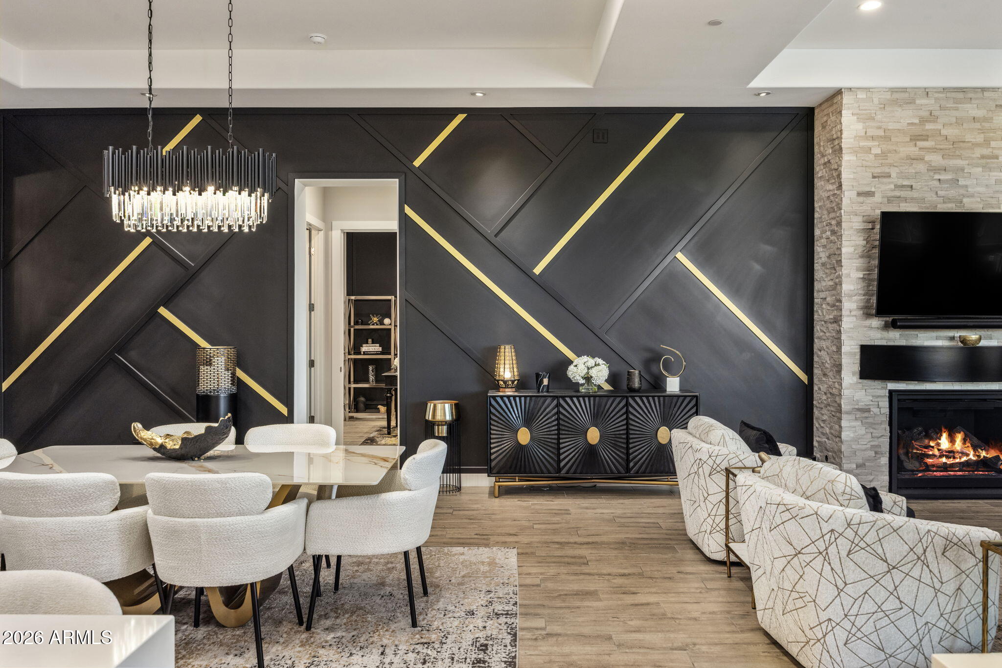 Open-plan dining and living room with a geometric charcoal-and-gold accent wall and stone fireplace.