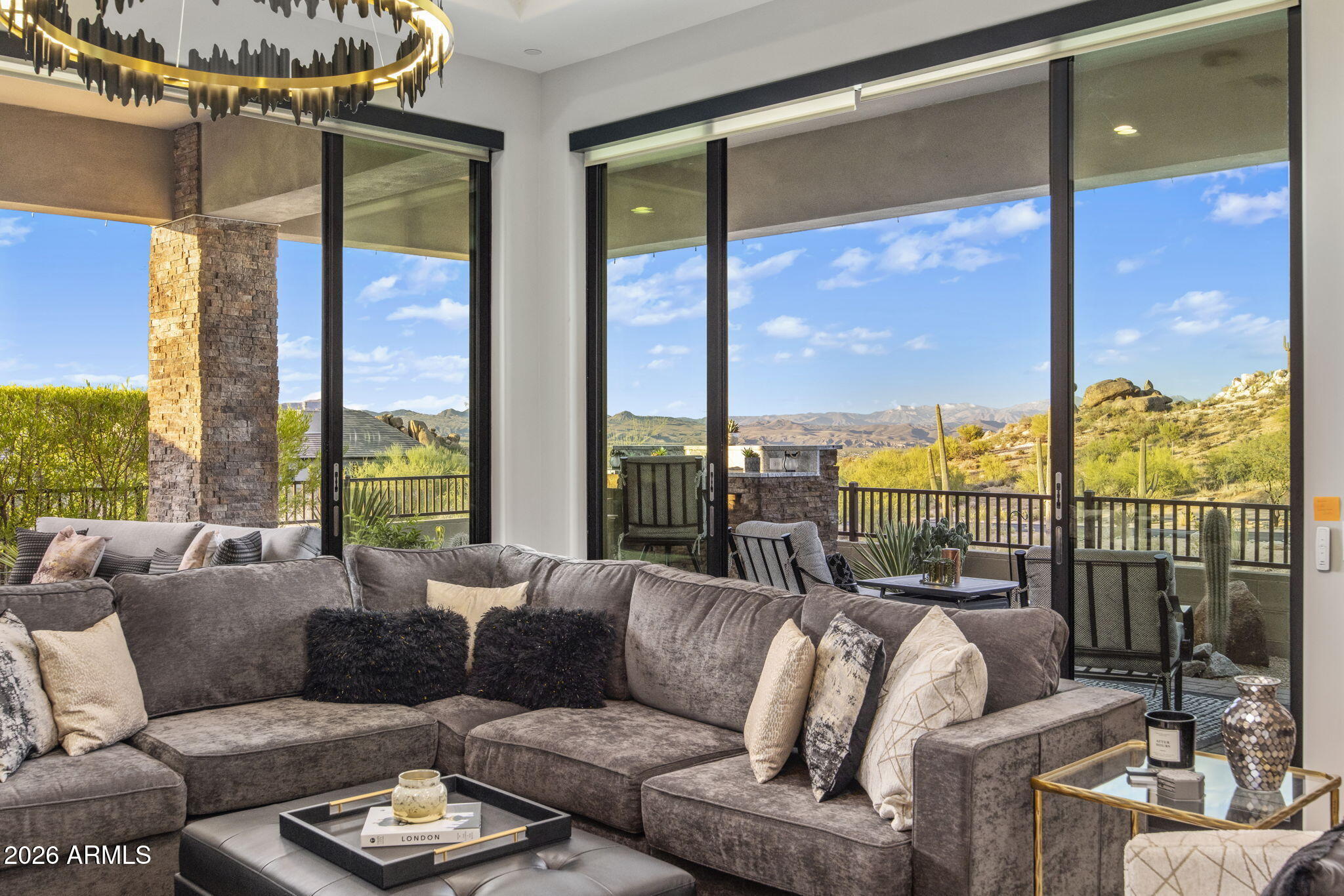 Living room with a gray sectional and floor-to-ceiling doors framing desert hills and mountain views.