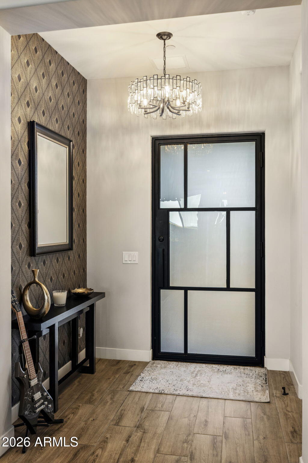 Foyer with a black-framed glass front door, crystal chandelier, and patterned accent wall.