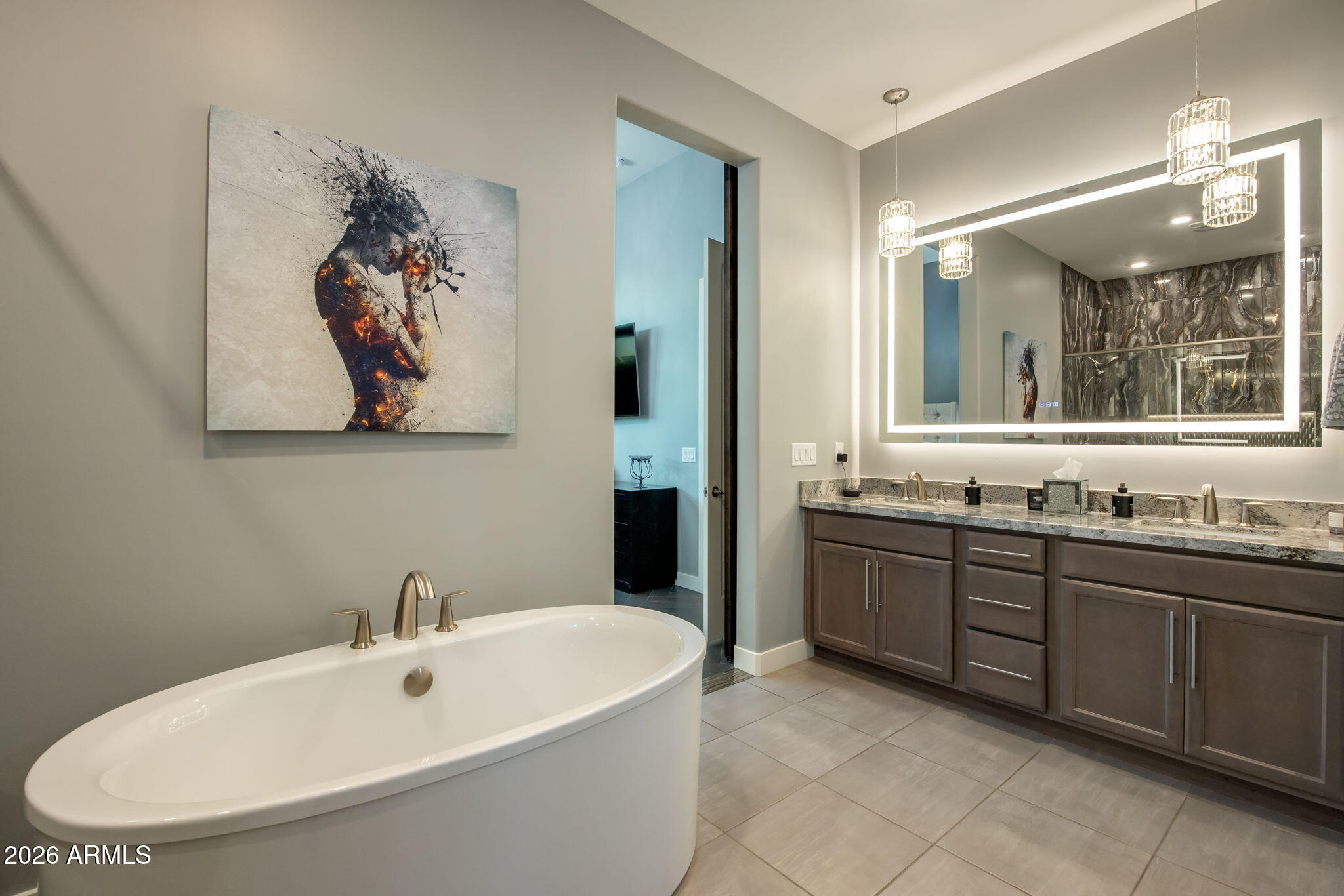 Modern bathroom with a freestanding tub and long double vanity beneath an illuminated mirror.