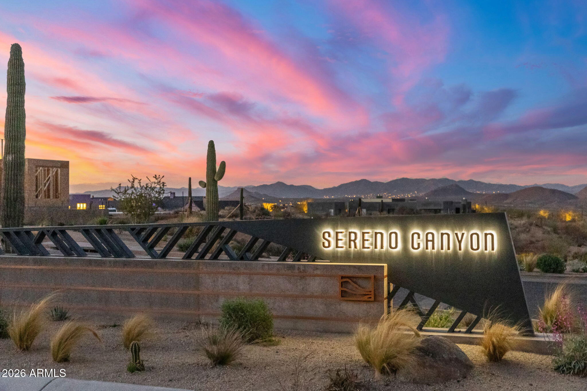 Sereno Canyon entrance sign among desert landscaping, with saguaro cacti and mountains at dusk.