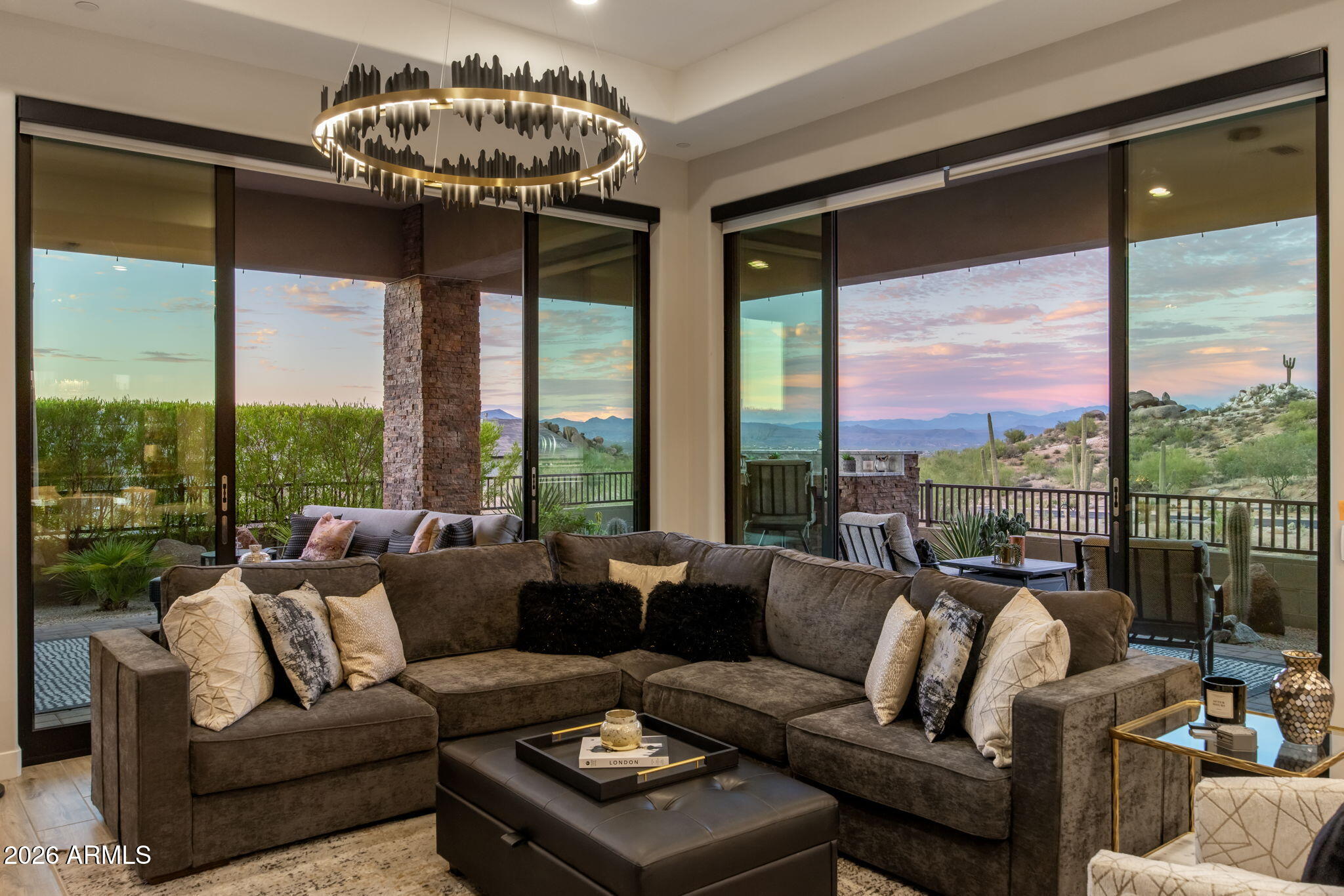 Living room with a brown sectional and wide windows overlooking desert mountains at dusk.