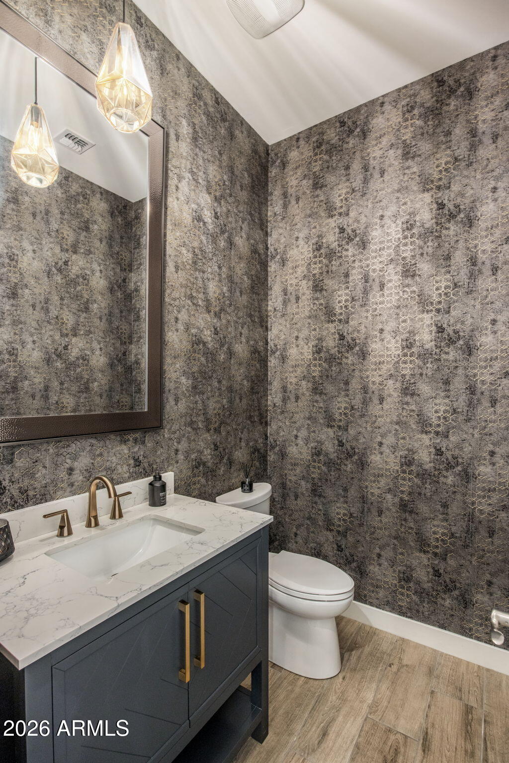 Powder room with patterned wallpaper, navy vanity, marble-look counter, brass fixtures, and geometric pendant lights.