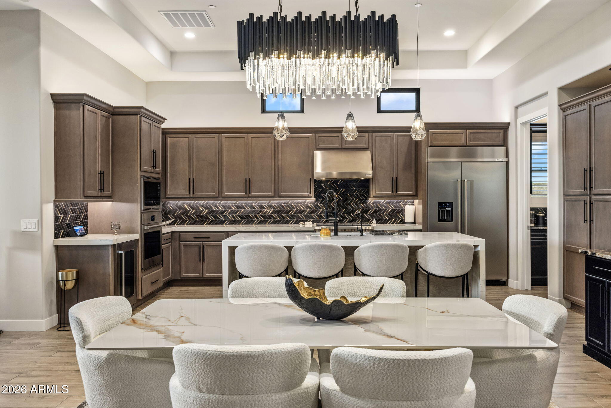 Furnished kitchen with dark cabinetry, herringbone backsplash, large island, and crystal chandelier.