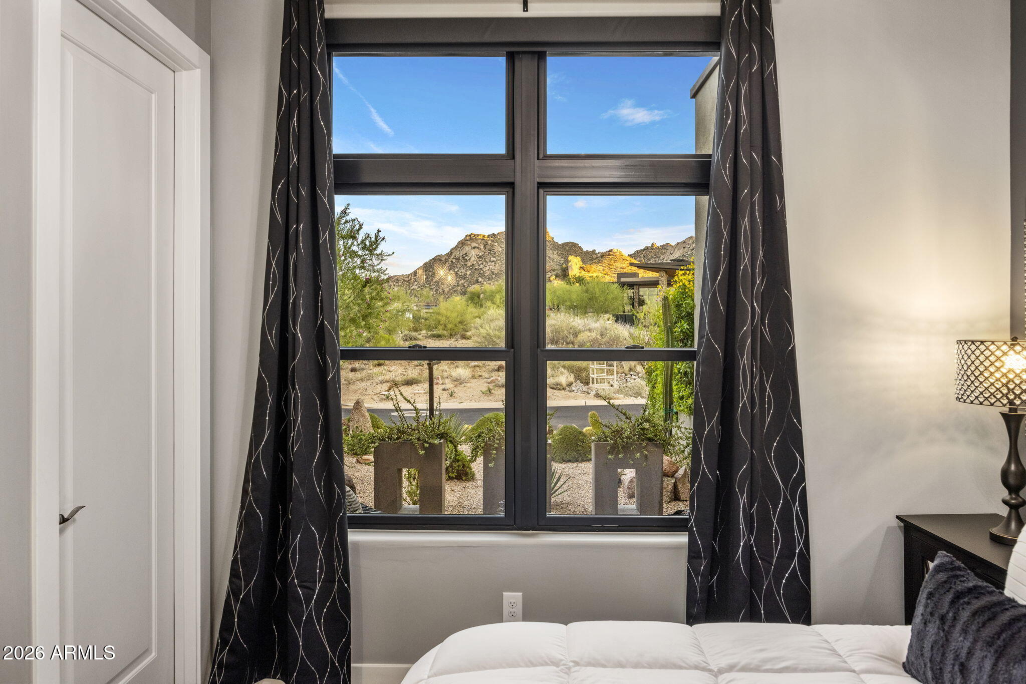 Bedroom with a large window overlooking desert landscaping and rocky mountains.