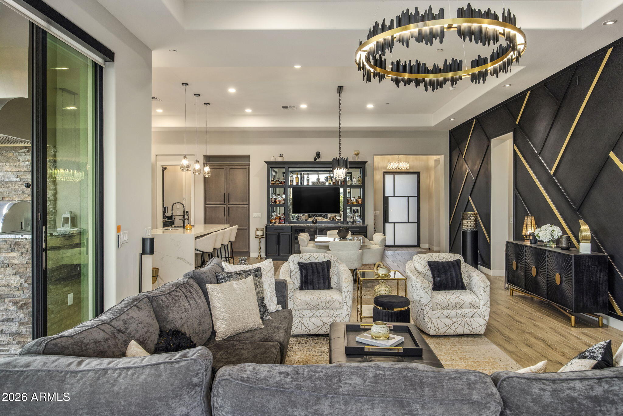 Living room with a sculptural ring chandelier, geometric black accent wall, and built-in bar.