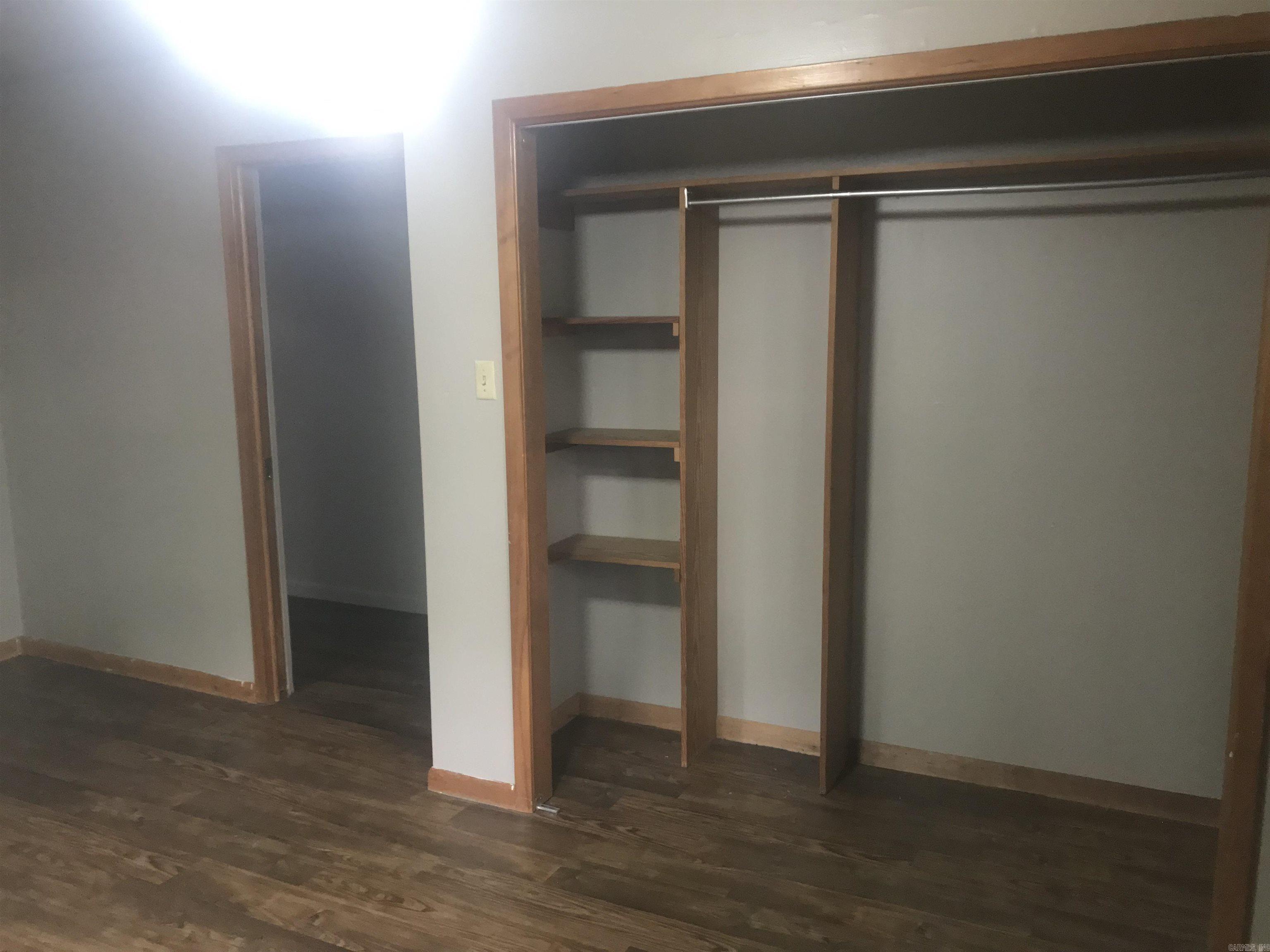 Empty bedroom closet with built-in shelves and hanging rod beside an open doorway.