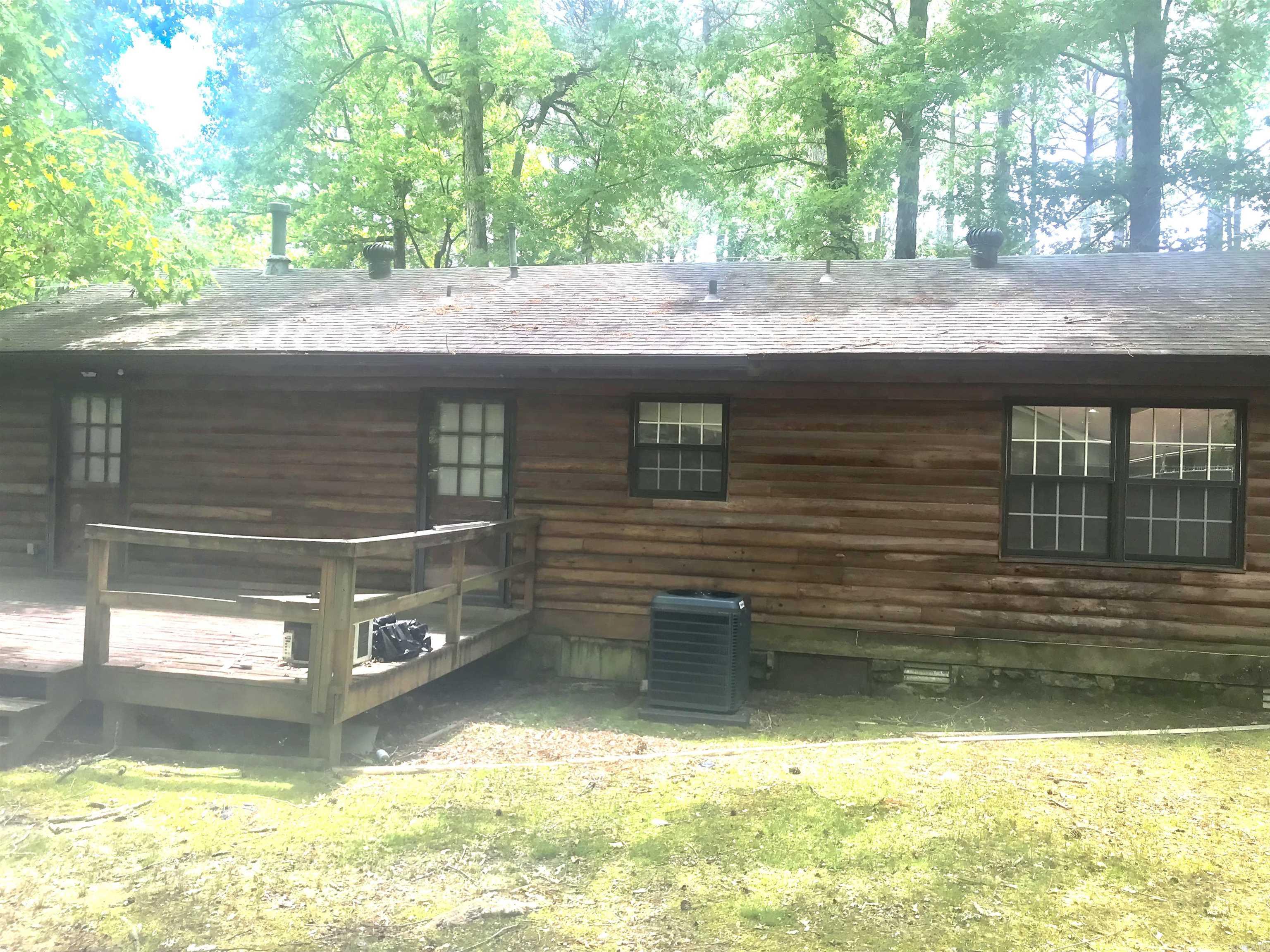 Rear of a log-sided house with a raised deck, dark-framed windows, and mature trees.
