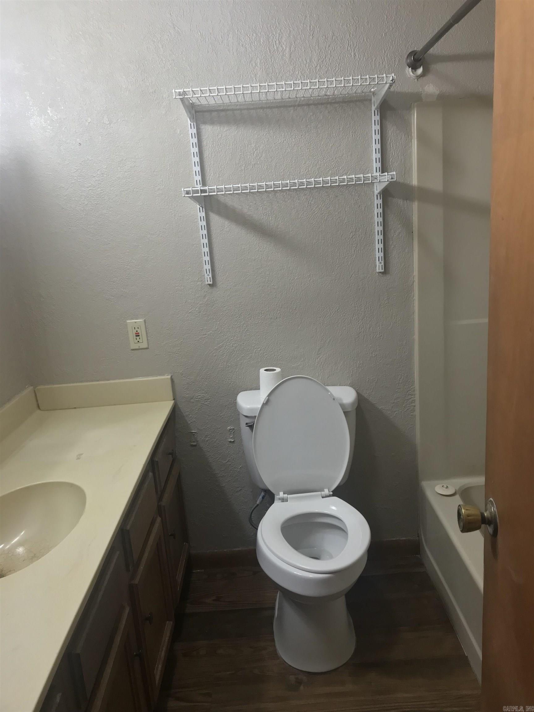 Bathroom with a white toilet, dark wood vanity, wire shelves, and a bathtub.
