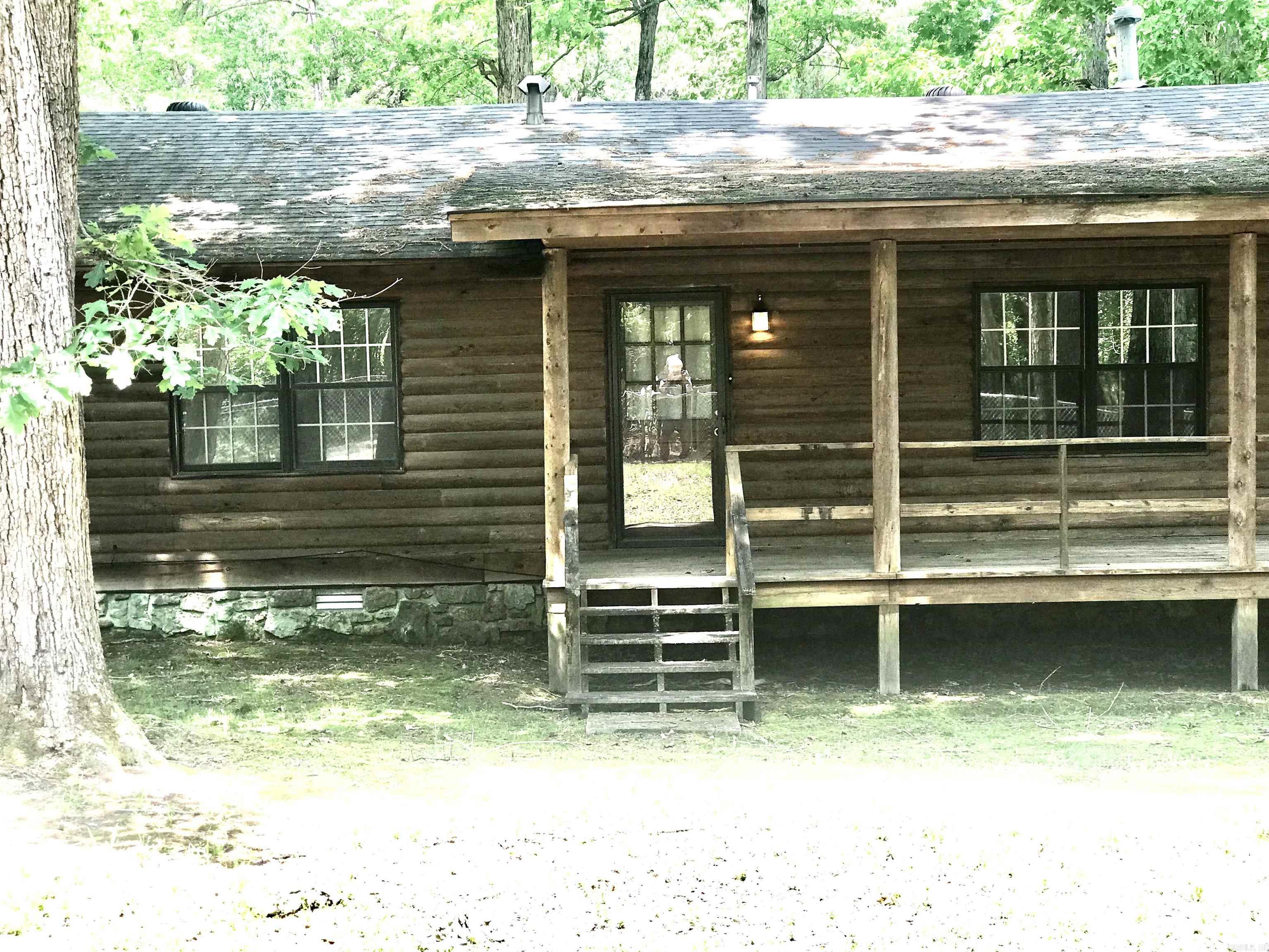 Rustic log cabin with a covered porch, central steps, and dark-framed windows beneath the trees.