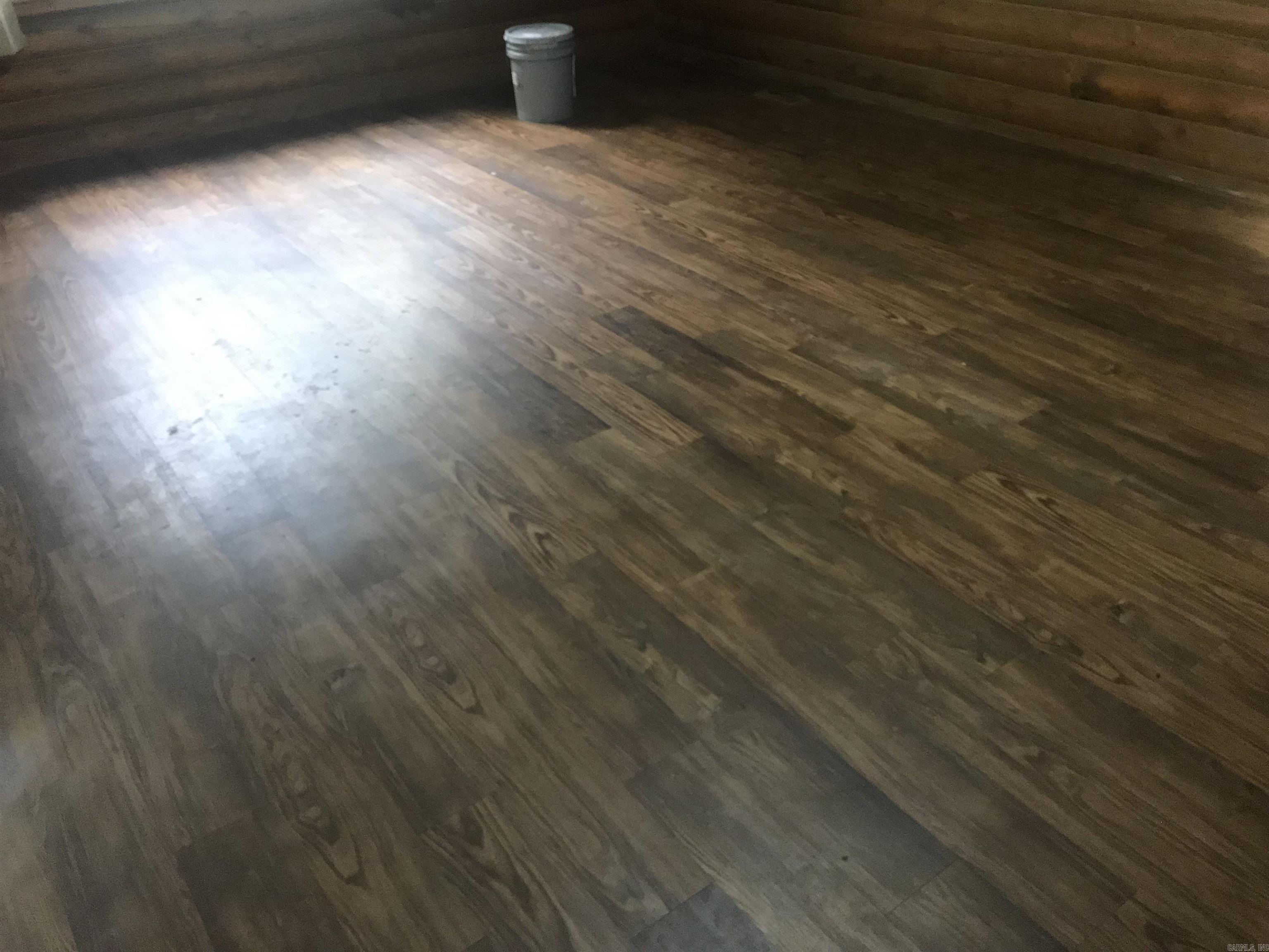 Room with worn wood-look flooring and a small bucket near the far wall.
