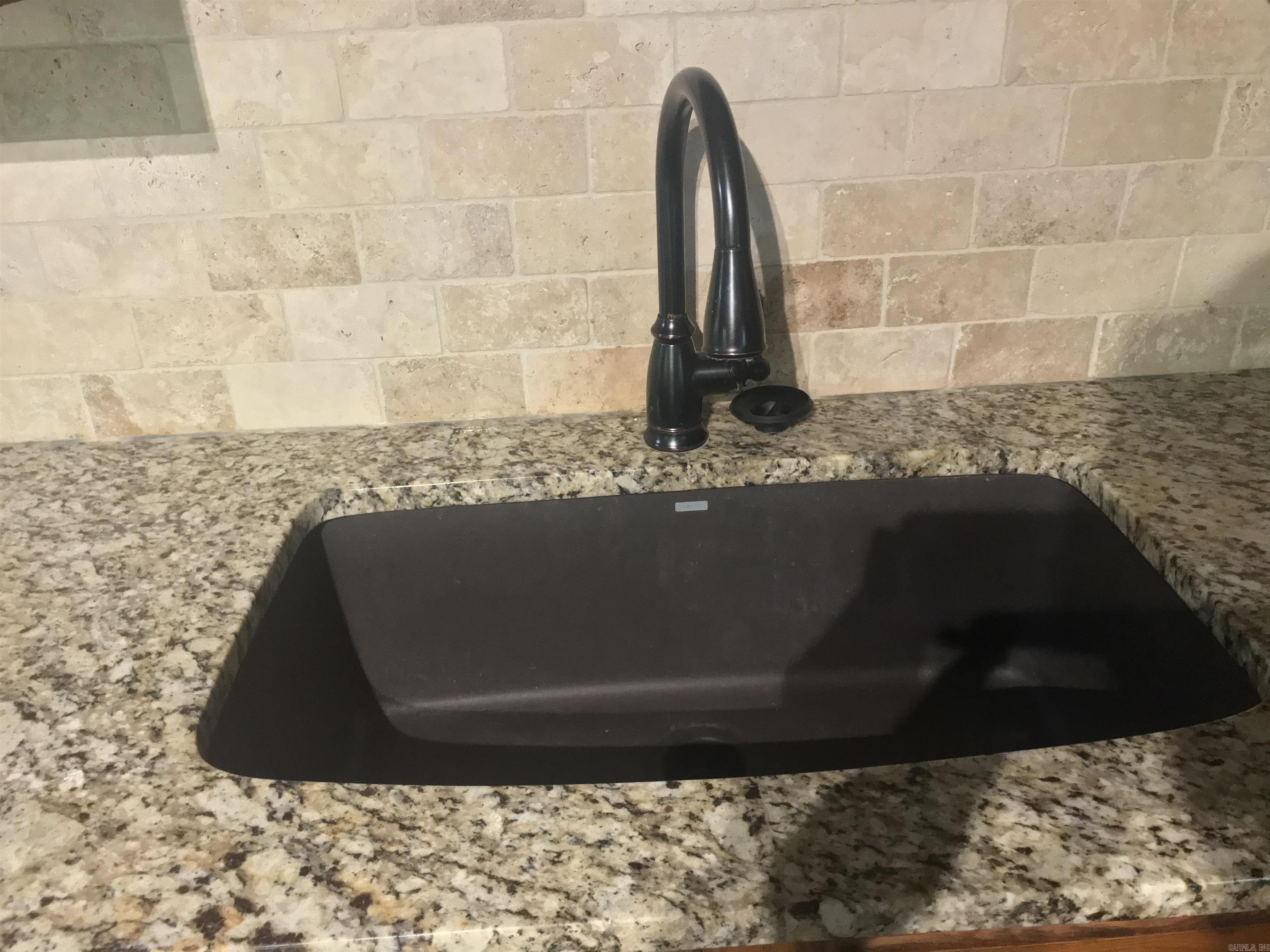 Kitchen sink with a black basin and faucet, granite countertops, and beige stone tile backsplash.