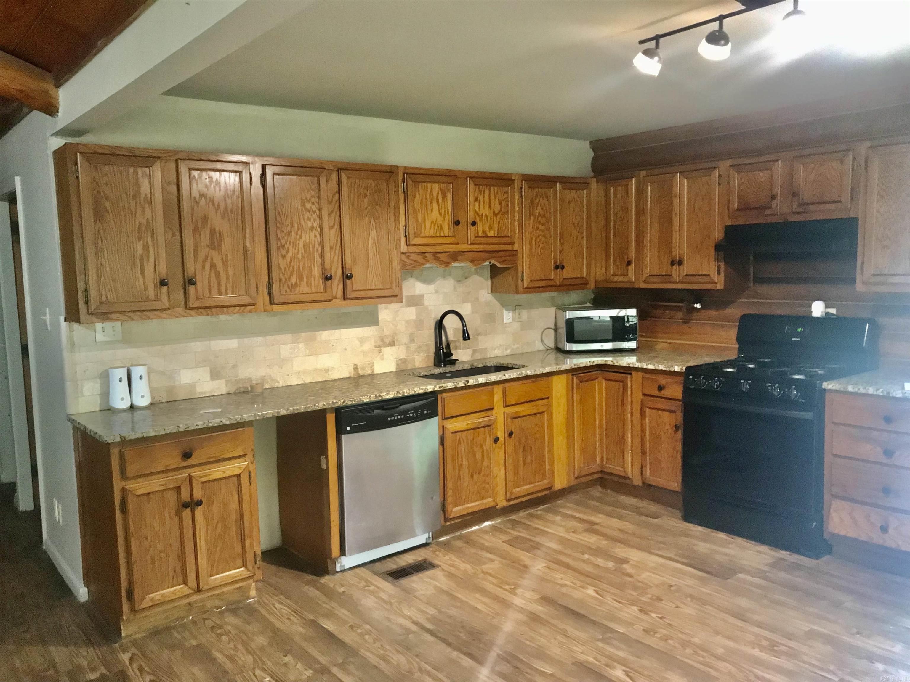Kitchen with oak cabinets, granite counters, stone tile backsplash, and black range.