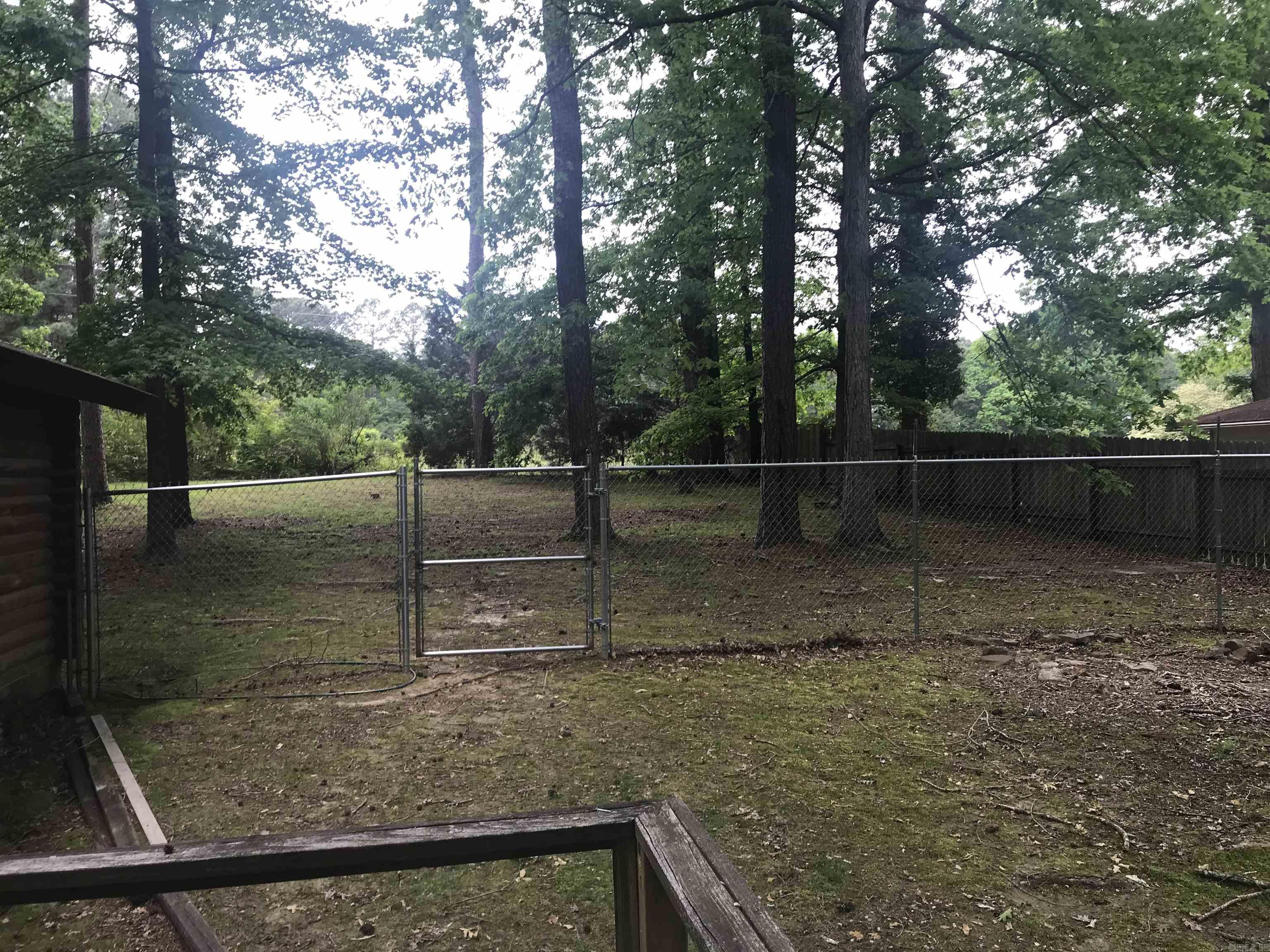 Shady backyard with a chain-link gate, mature trees, and a wooden privacy fence.