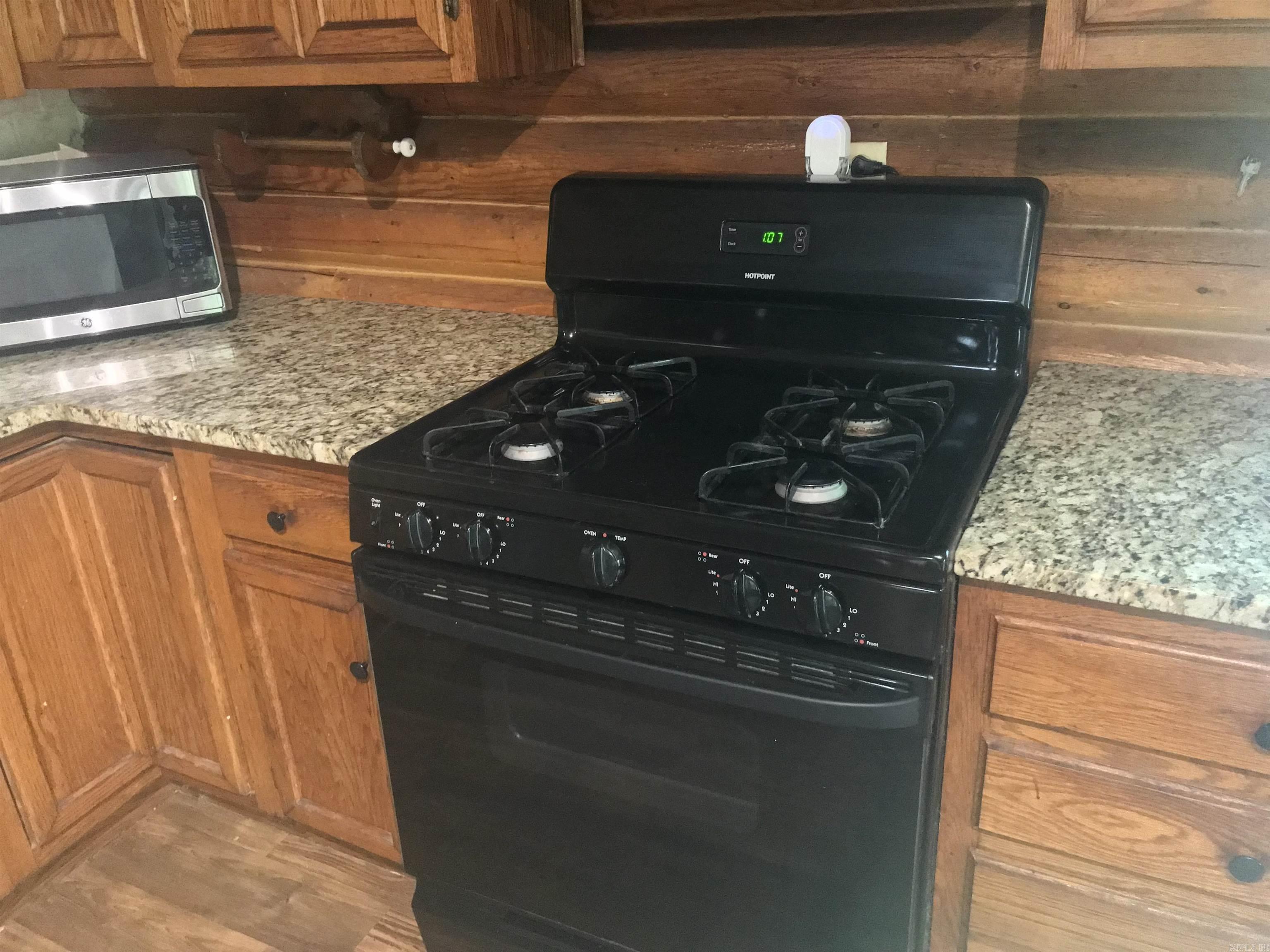 Kitchen with a black gas range, granite counters, and warm wood cabinetry and walls.