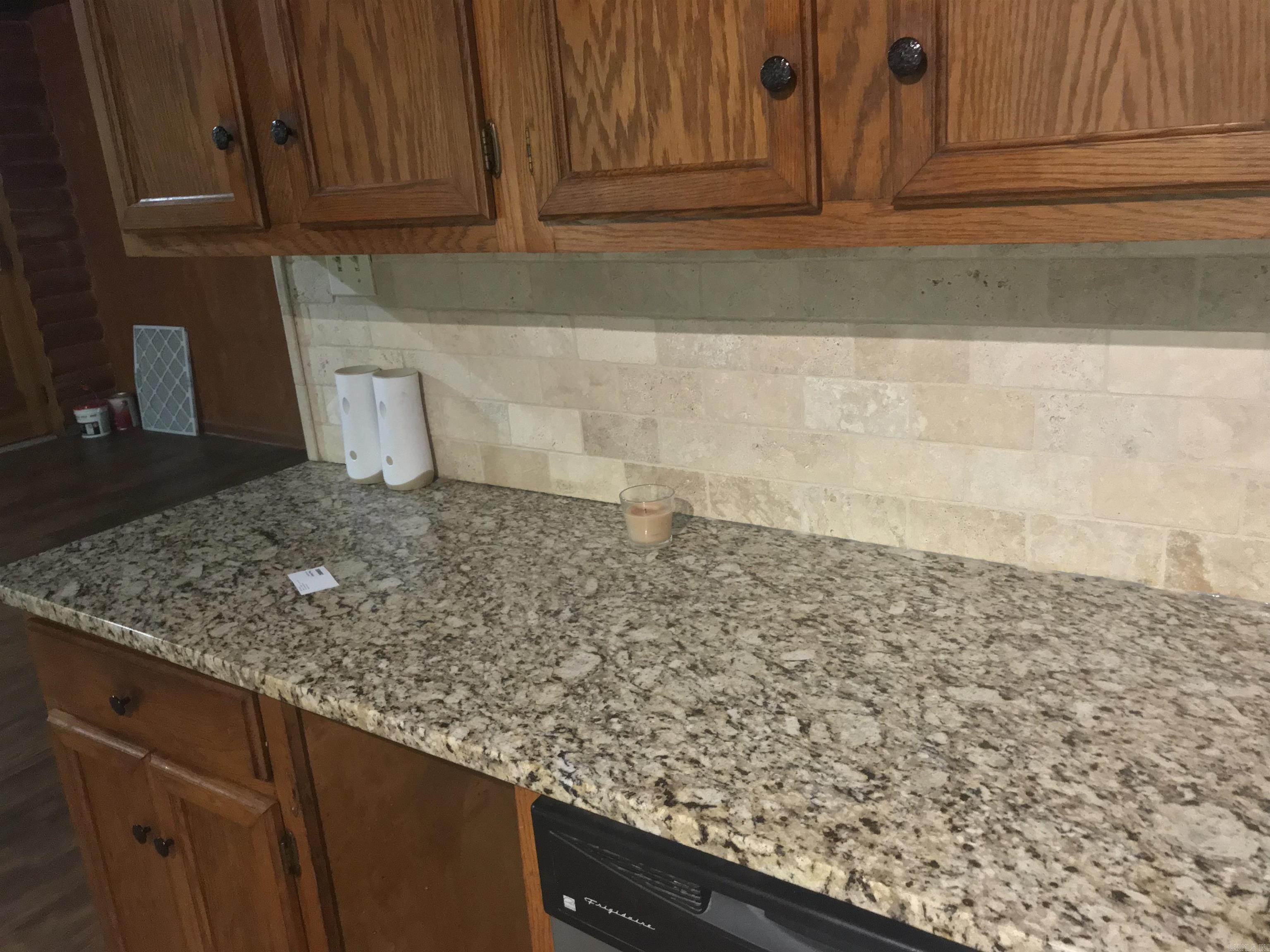 Kitchen with speckled granite counters, wood cabinets, stone backsplash, and a built-in dishwasher.