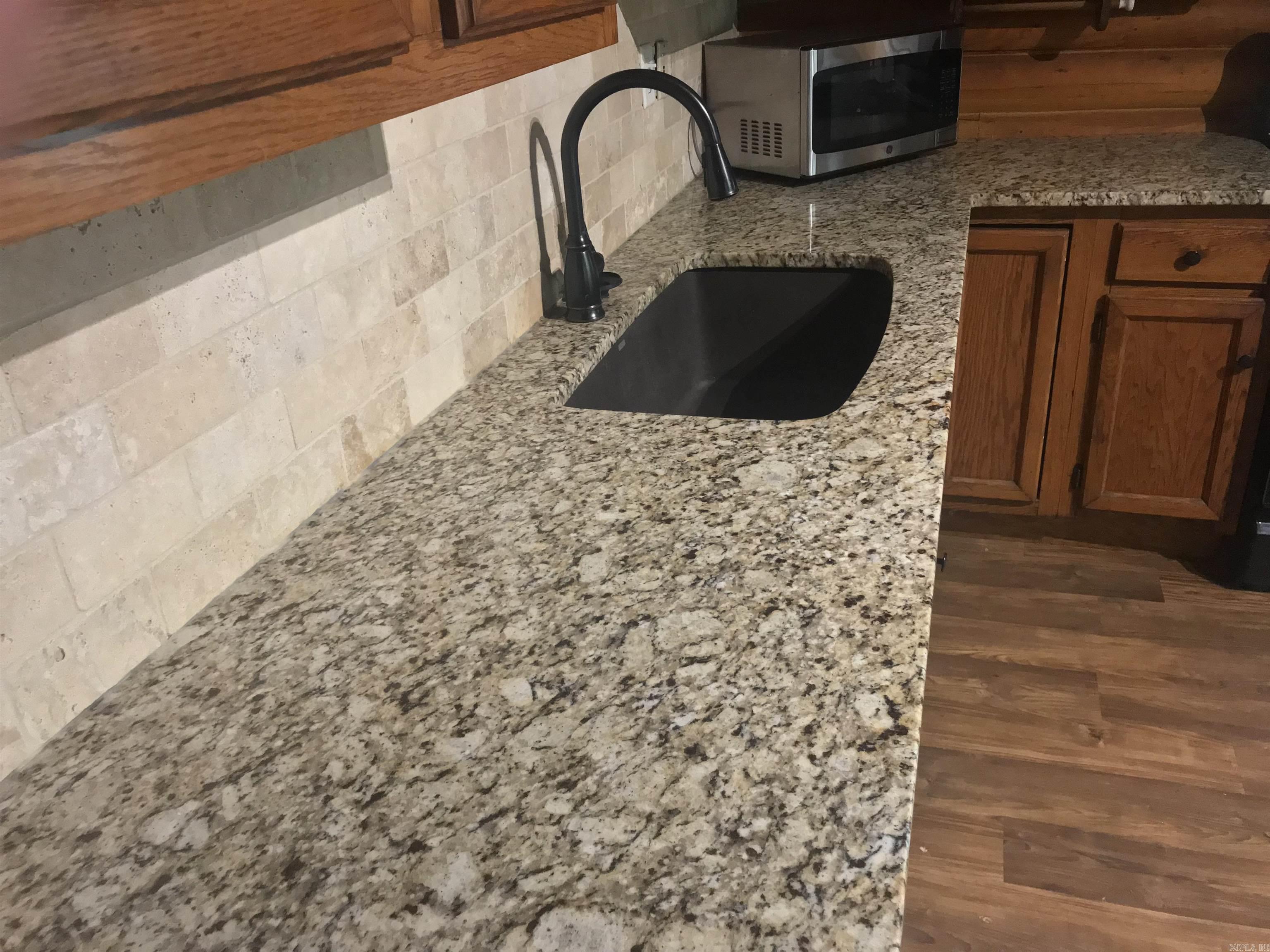 Kitchen granite countertop with black sink and faucet, stone tile backsplash, and warm wood cabinets.