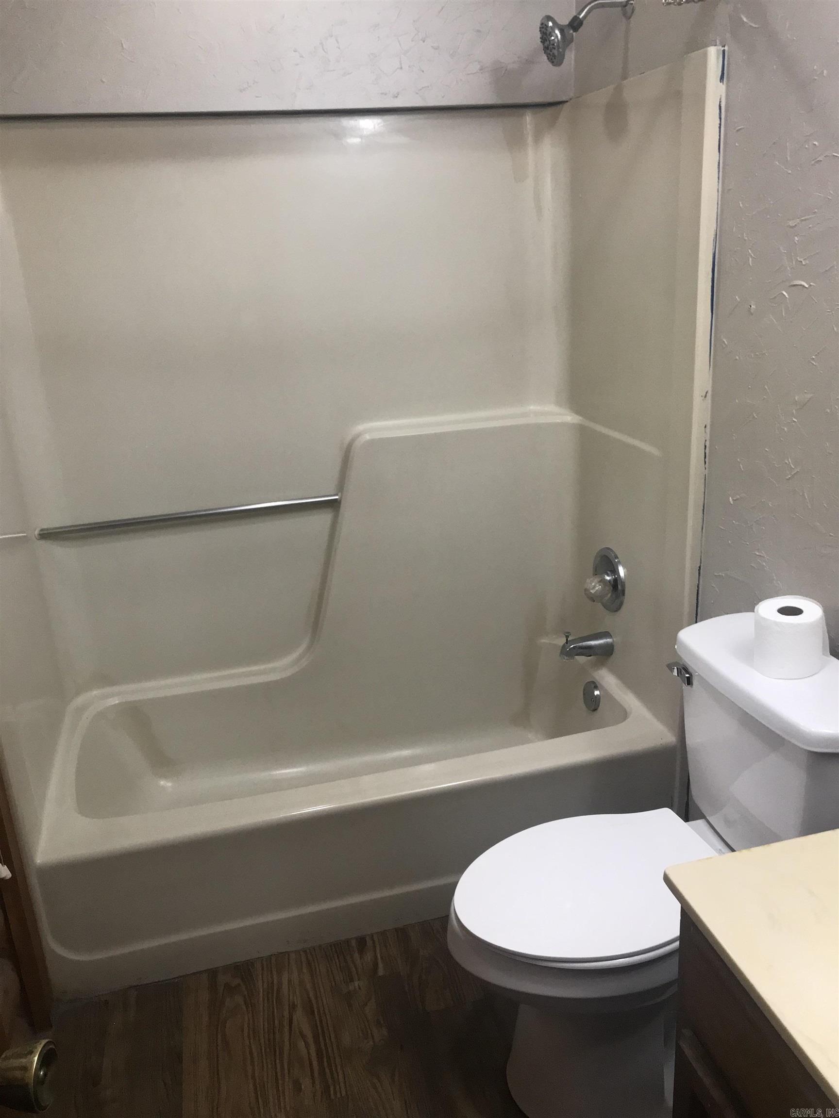 Bathroom with a beige tub and shower, chrome grab bar, and white toilet.