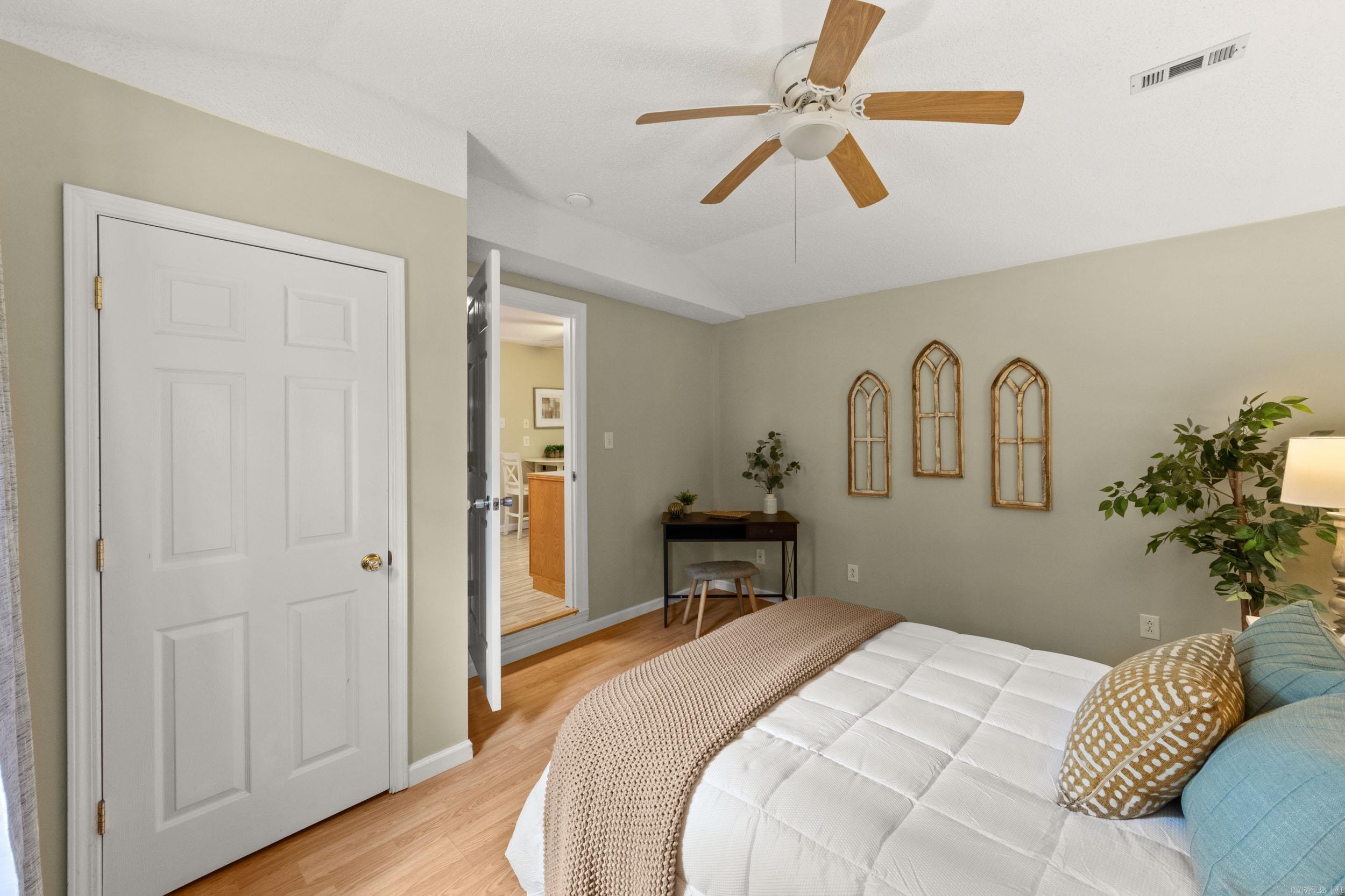 Furnished bedroom with a ceiling fan, light wood floors, and three arched wall accents.