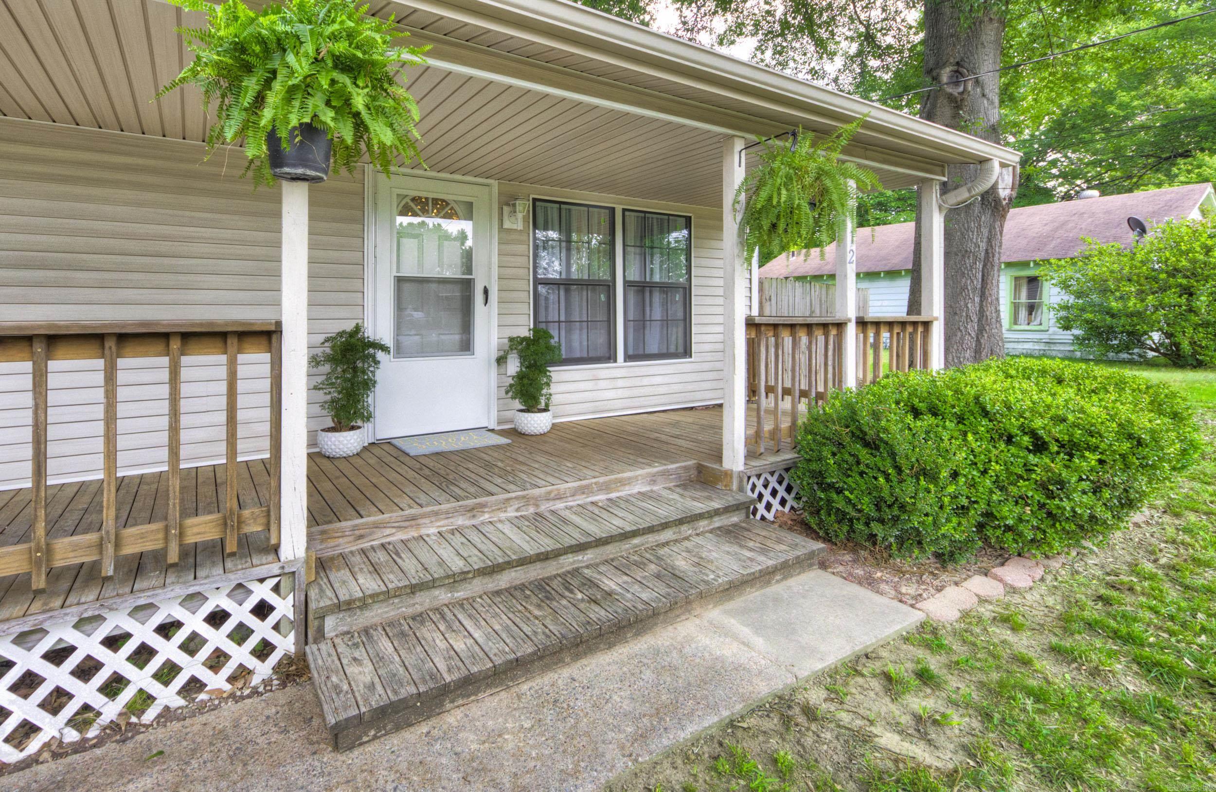 Home’s covered front porch with wide wooden steps, hanging ferns, and potted plants by the entry.