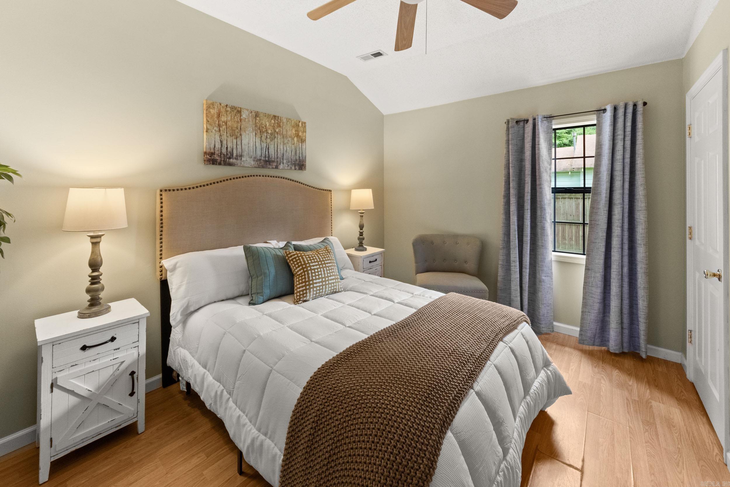 Staged bedroom with a large bed, brown knit throw, gray curtains, and wood-look flooring.