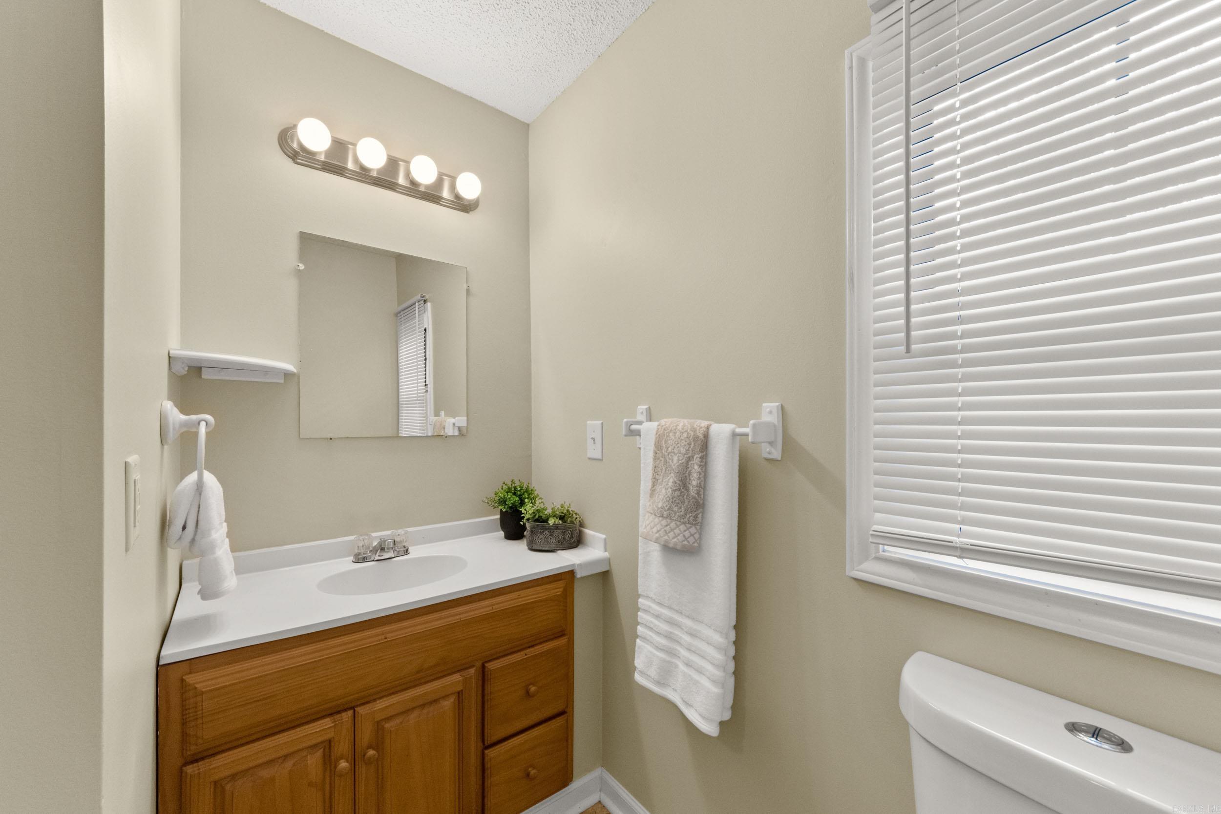 Bathroom with a wood vanity, white sink, large window with closed blinds, and part of a toilet.