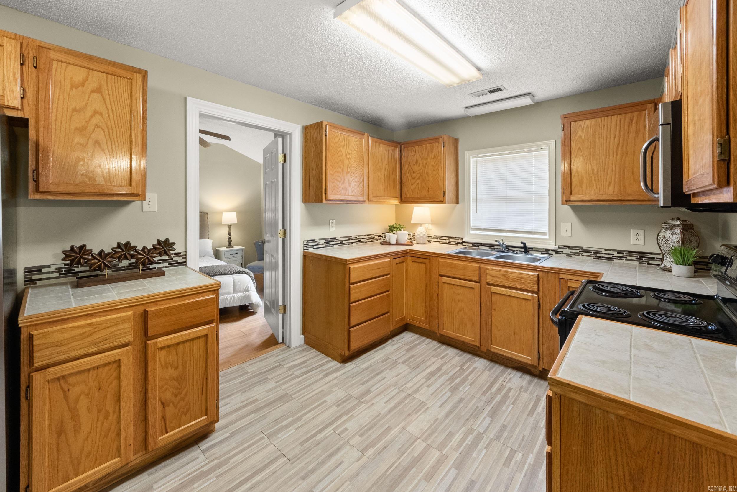 Kitchen with honey-colored wood cabinets, tiled counters, and a sink beneath a window.