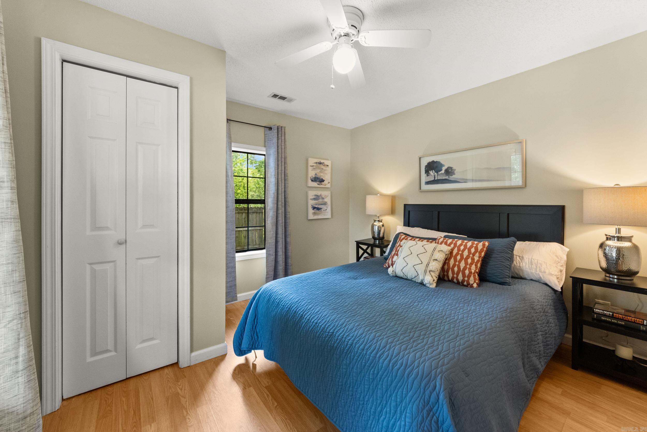 Bedroom with a blue quilted bed, dark headboard, hardwood floors, and a curtained window.