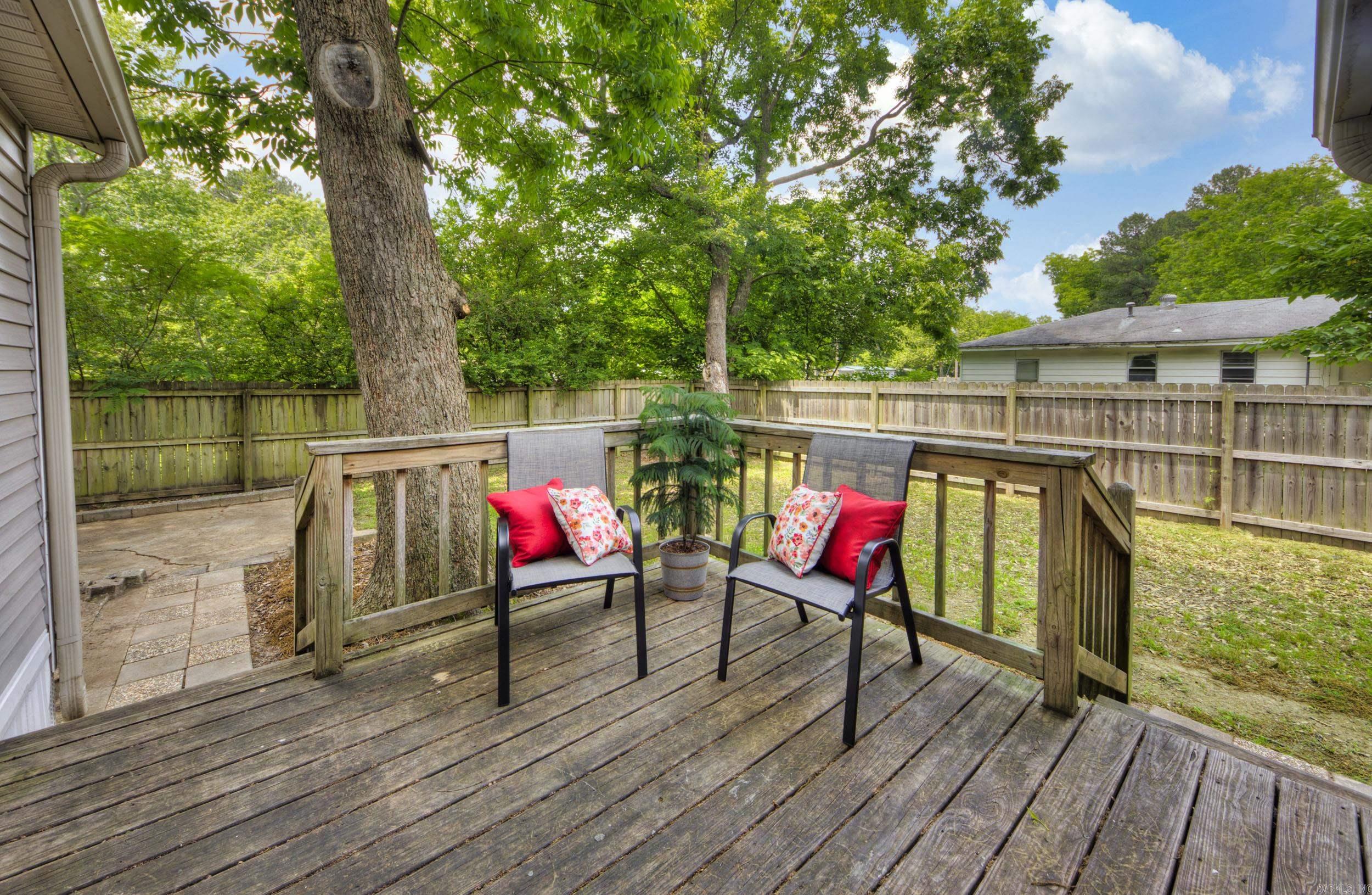 Wooden backyard deck with two cushioned chairs, mature trees, and a fenced yard.