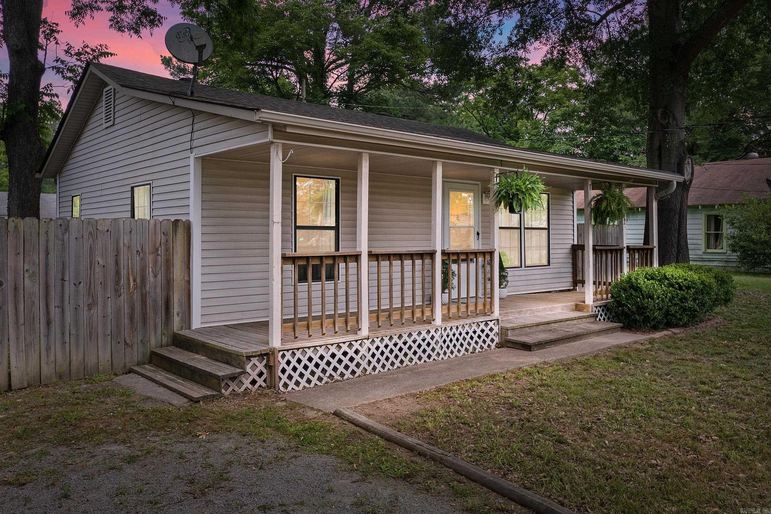 Gray-sided home with a long covered porch, hanging ferns, and white lattice skirting at dusk.