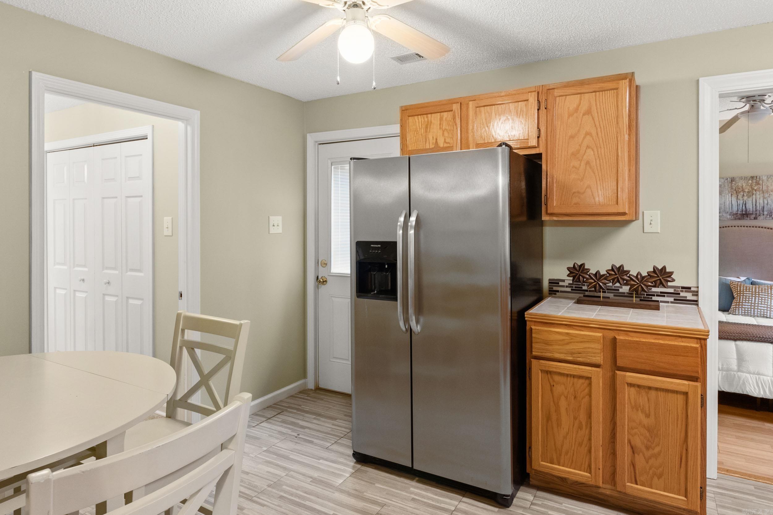 Kitchen with wood cabinets, stainless steel refrigerator, tiled counter, and adjoining dining area.
